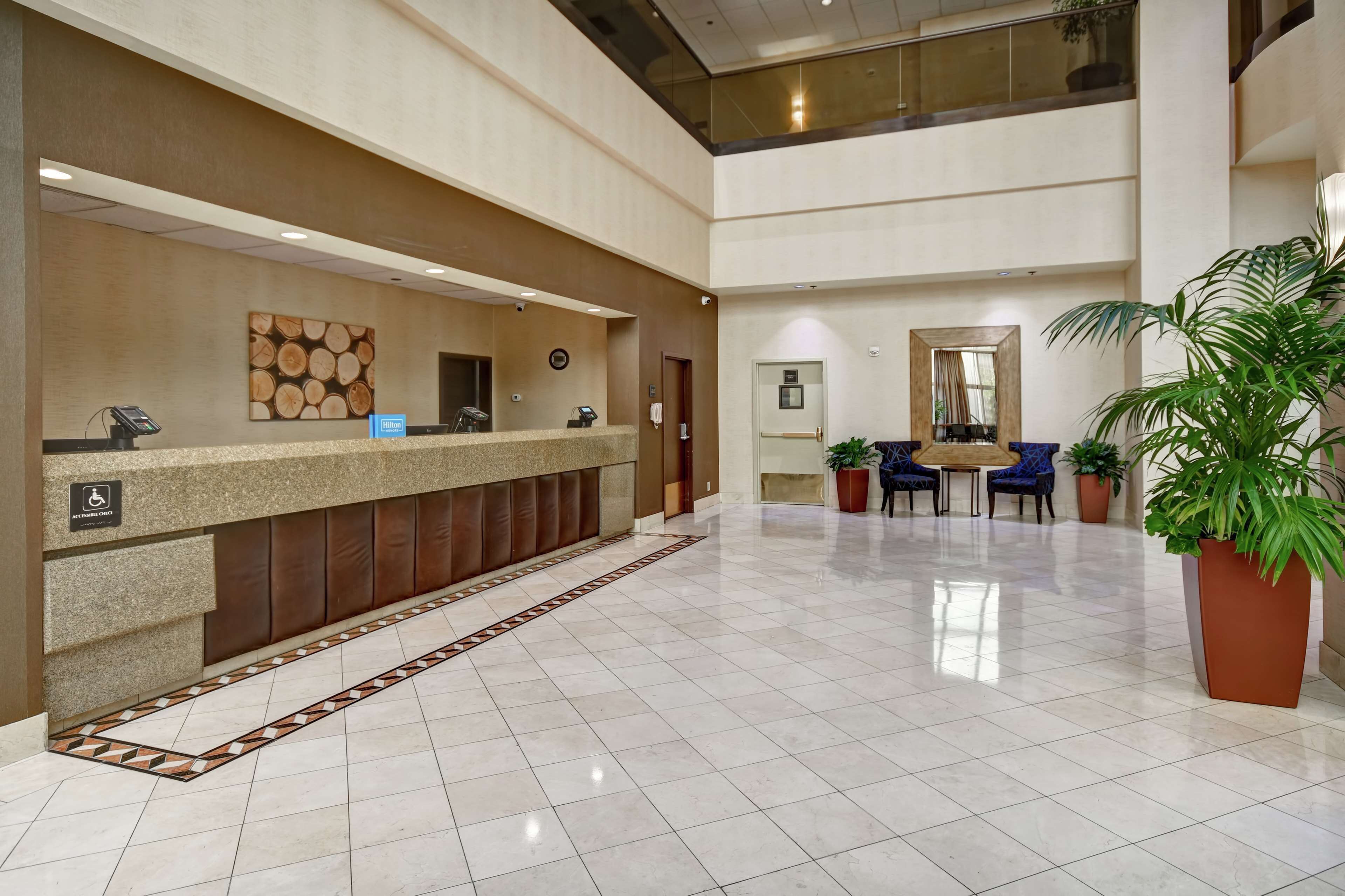 Zona de recepción de hotel con mostrador, un reloj y un área de estar con sillas y una mesa.