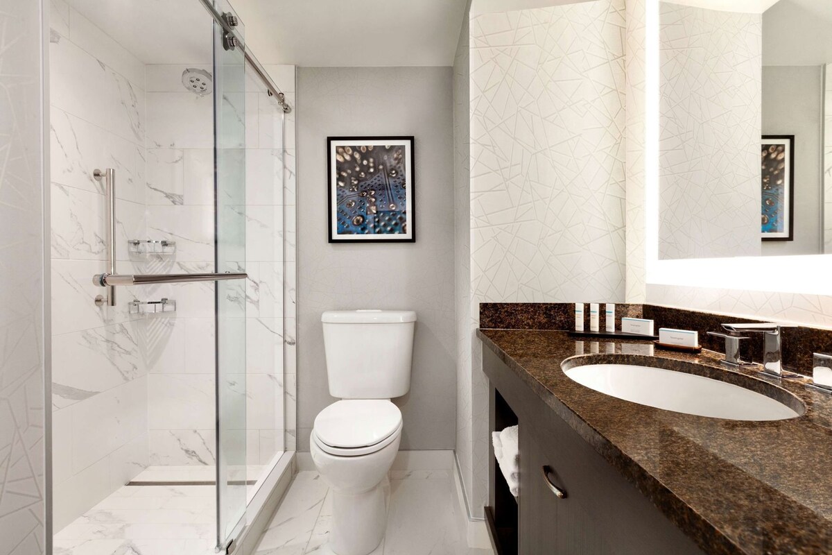 Een moderne badkamer met een douchecabine van glas, een wit toilet en een wastafel met spiegel op een granieten aanrecht.