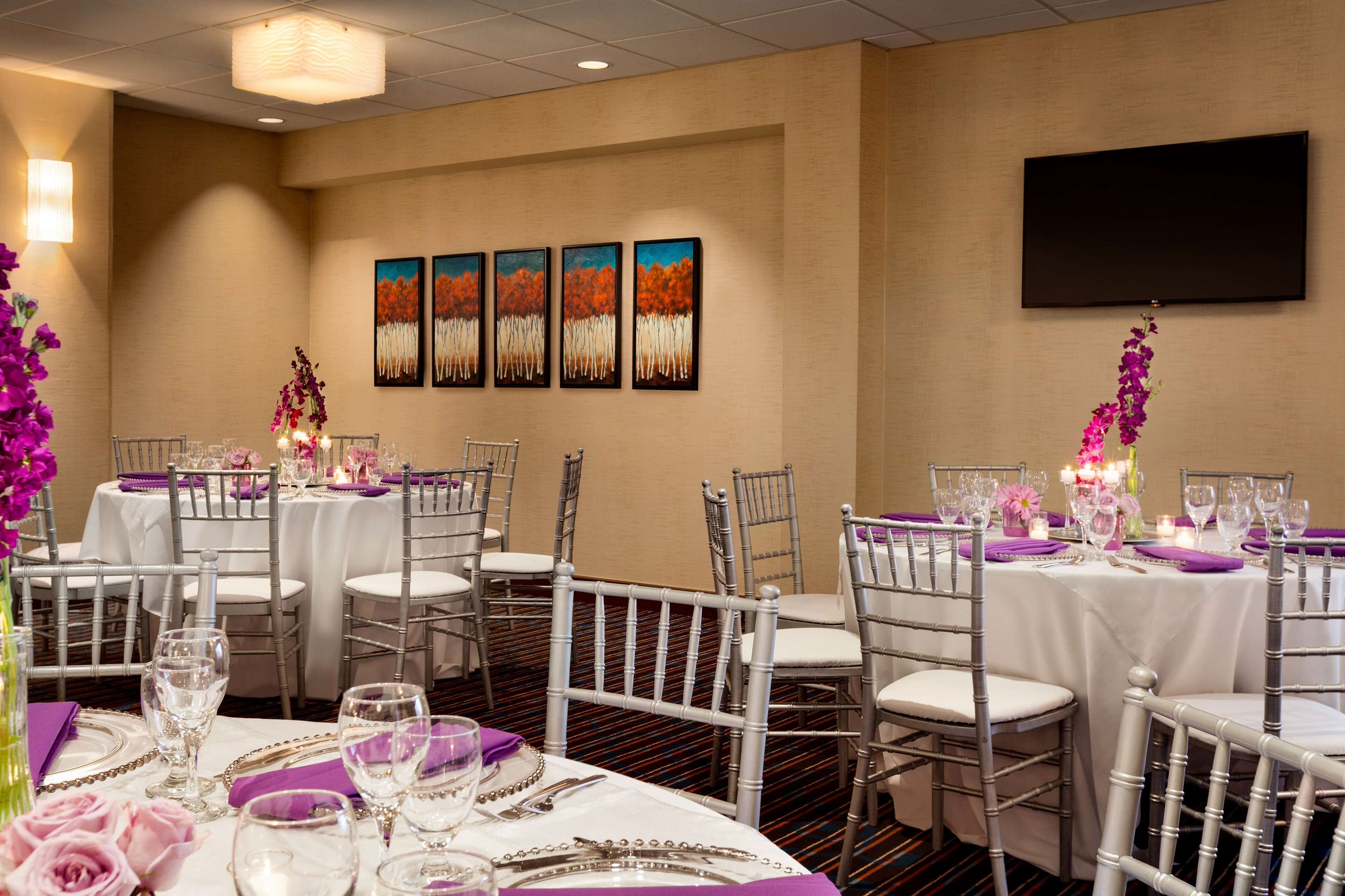 A banquet hall with round tables, white tablecloths, and purple napkins.