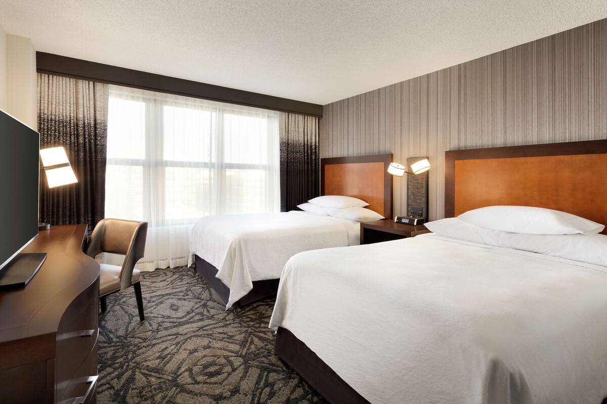 A hotel room with two beds, a desk, and a chair.