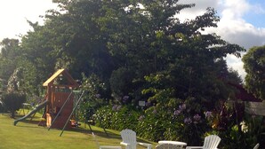 A playground with a slide and a swing set, surrounded by lush greenery and flowering plants.