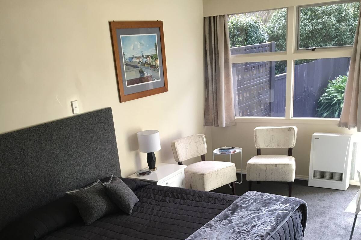 Habitación de hotel con una cama grande, un escritorio, una silla, una mesita y una ventana con cortinas.