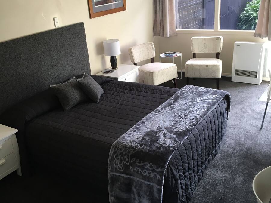 A hotel room with a large bed, a desk, a chair, a small table, and a window with curtains.