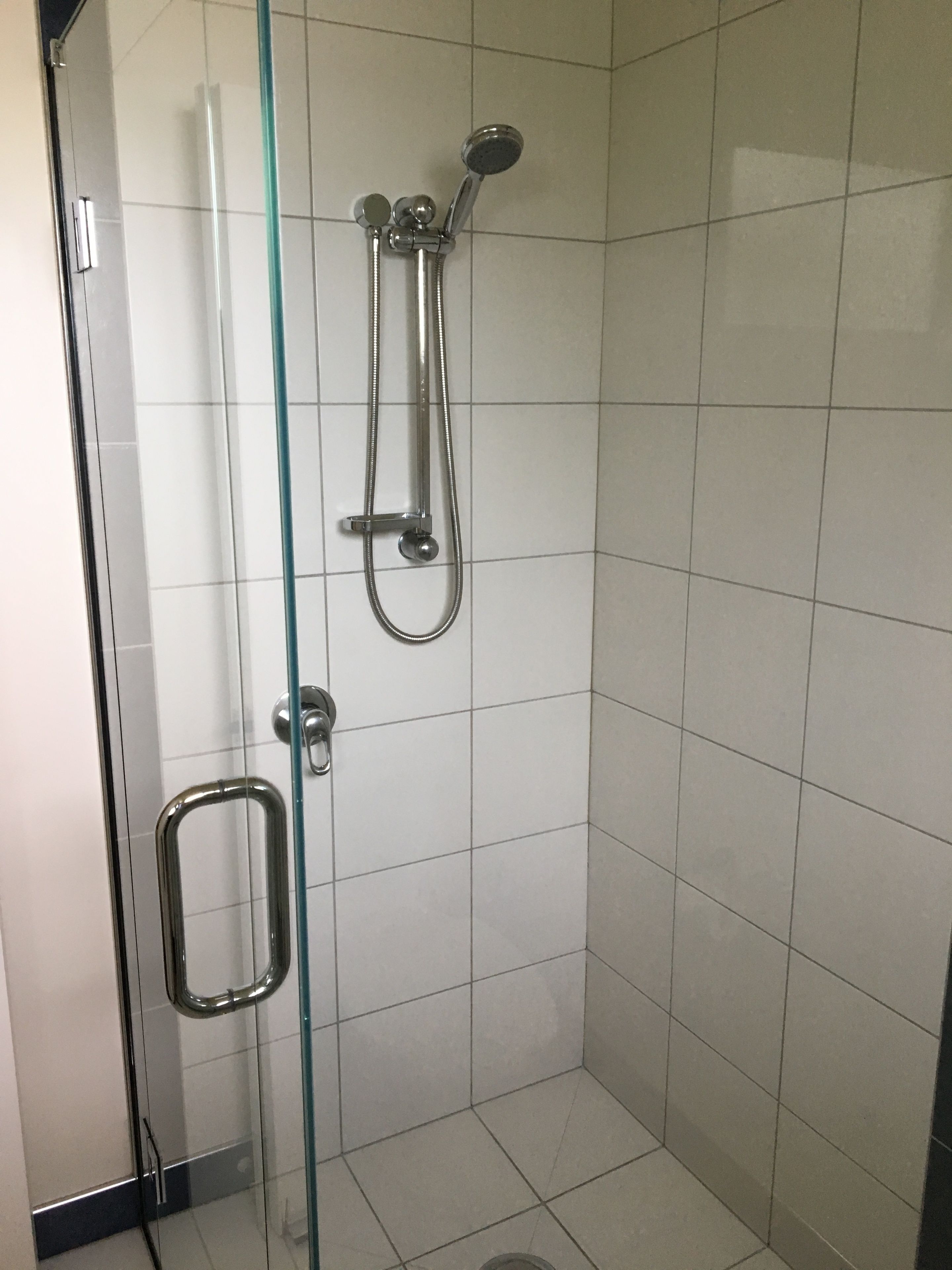 A glass-enclosed shower stall with a handheld showerhead and a fixed showerhead.
