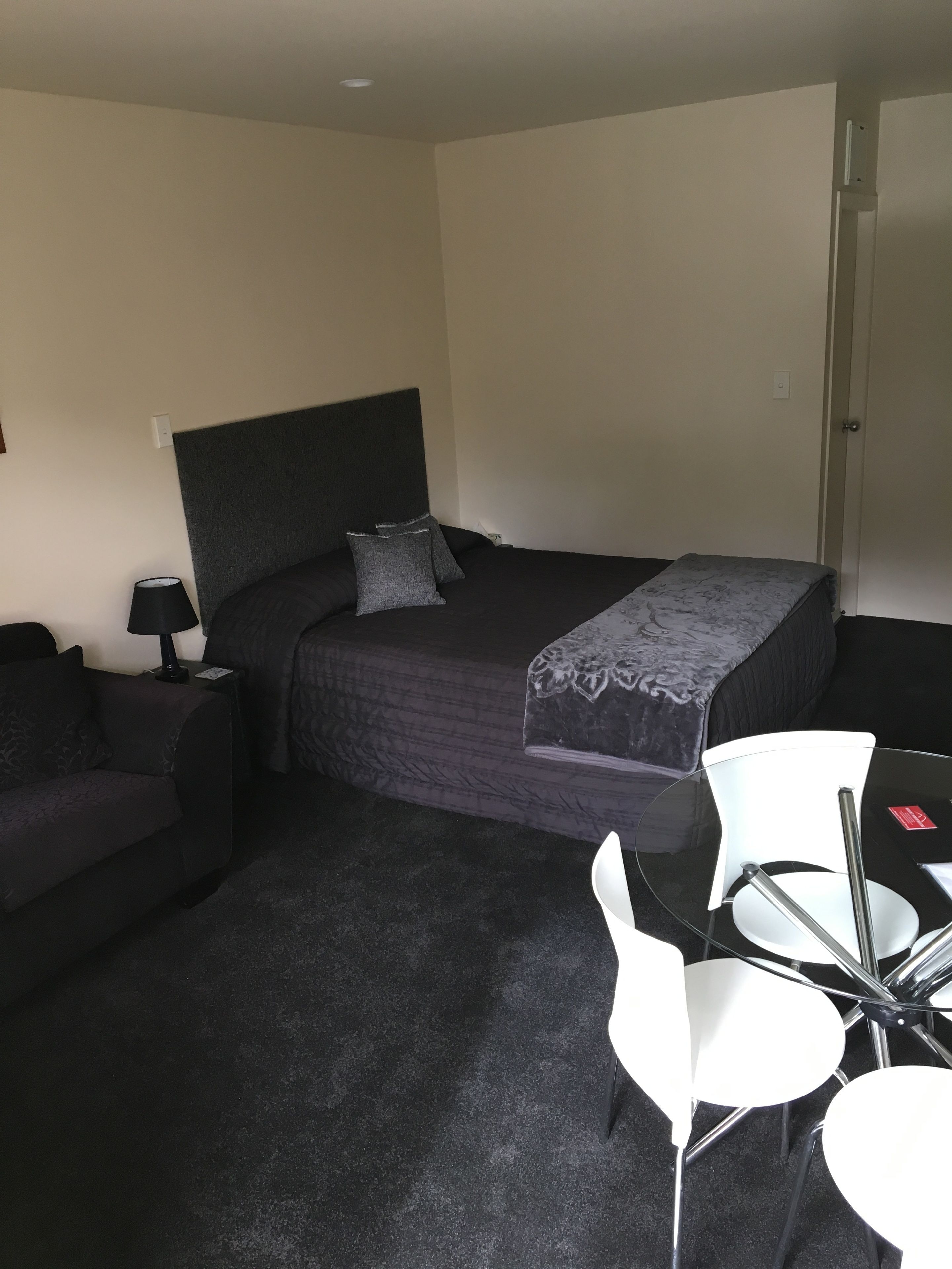 A bedroom with a bed, bedside table, lamp, and a small seating area with chairs.