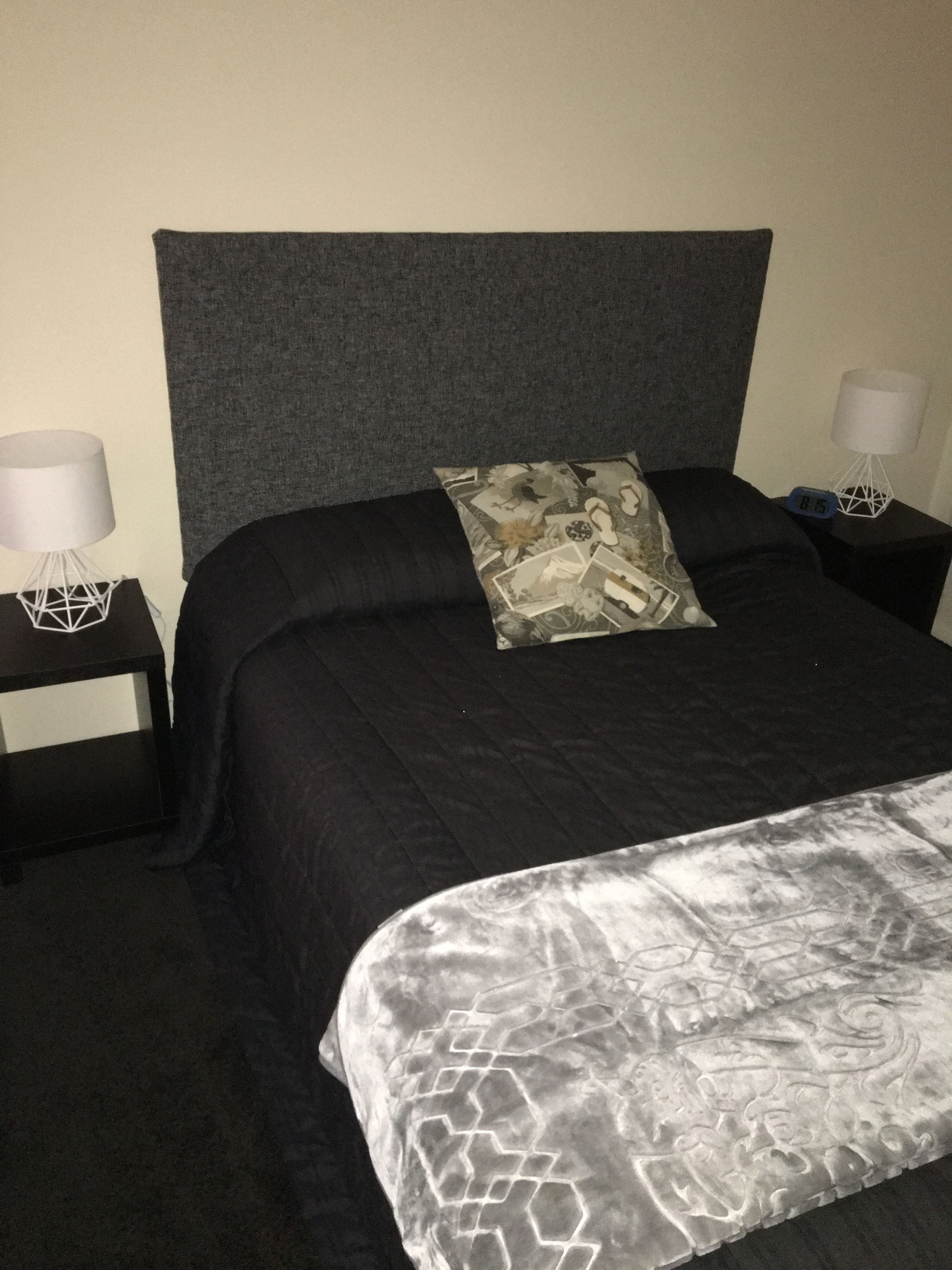 A neatly made bed with a patterned pillow, black headboard, and a grey patterned bedspread. There are two bedside tables with lamps and a clock on one of them.