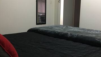 A bedroom with a bed, a red pillow, a mirror, and a door.