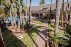 A resort with a pool area, palm trees, and a pathway leading to the building. - La Copa Hotel (McAllen)