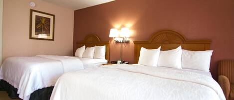 A hotel room with two beds, a nightstand, a lamp, and a framed picture on the wall.