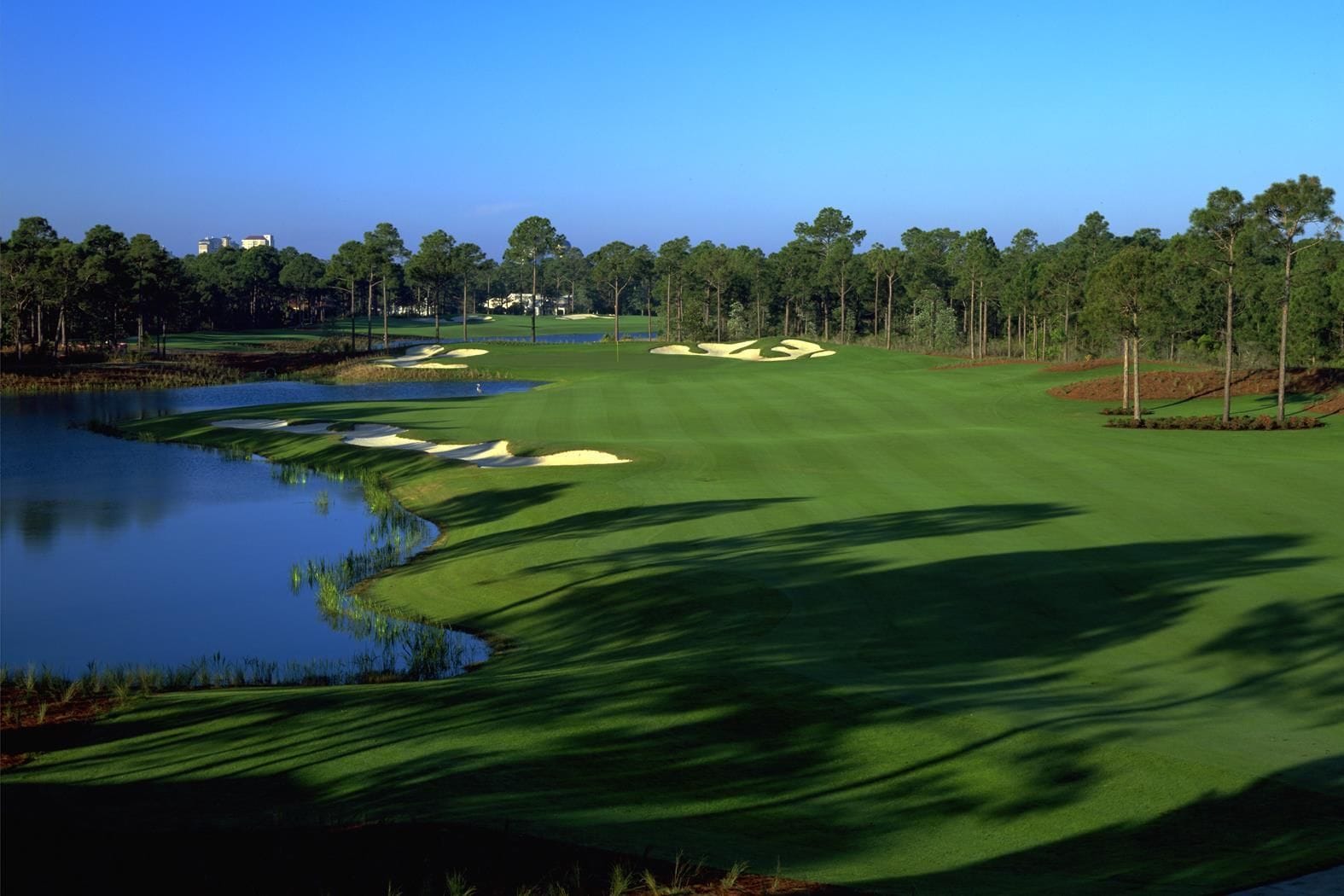 A golf course with a water hazard, sand bunkers, and a forested area.