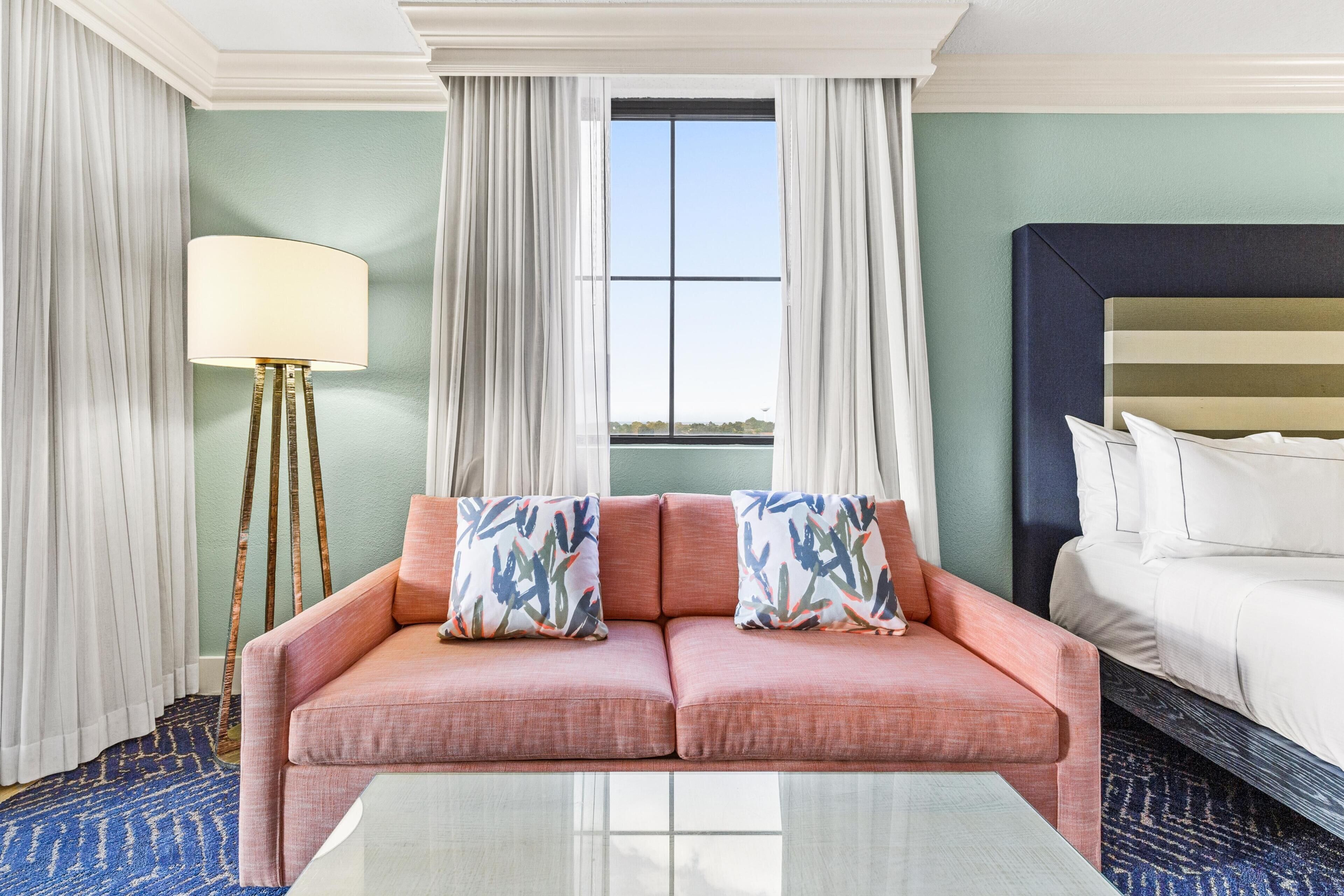 A hotel room with a sofa, a bed, a lamp, and a window with curtains.