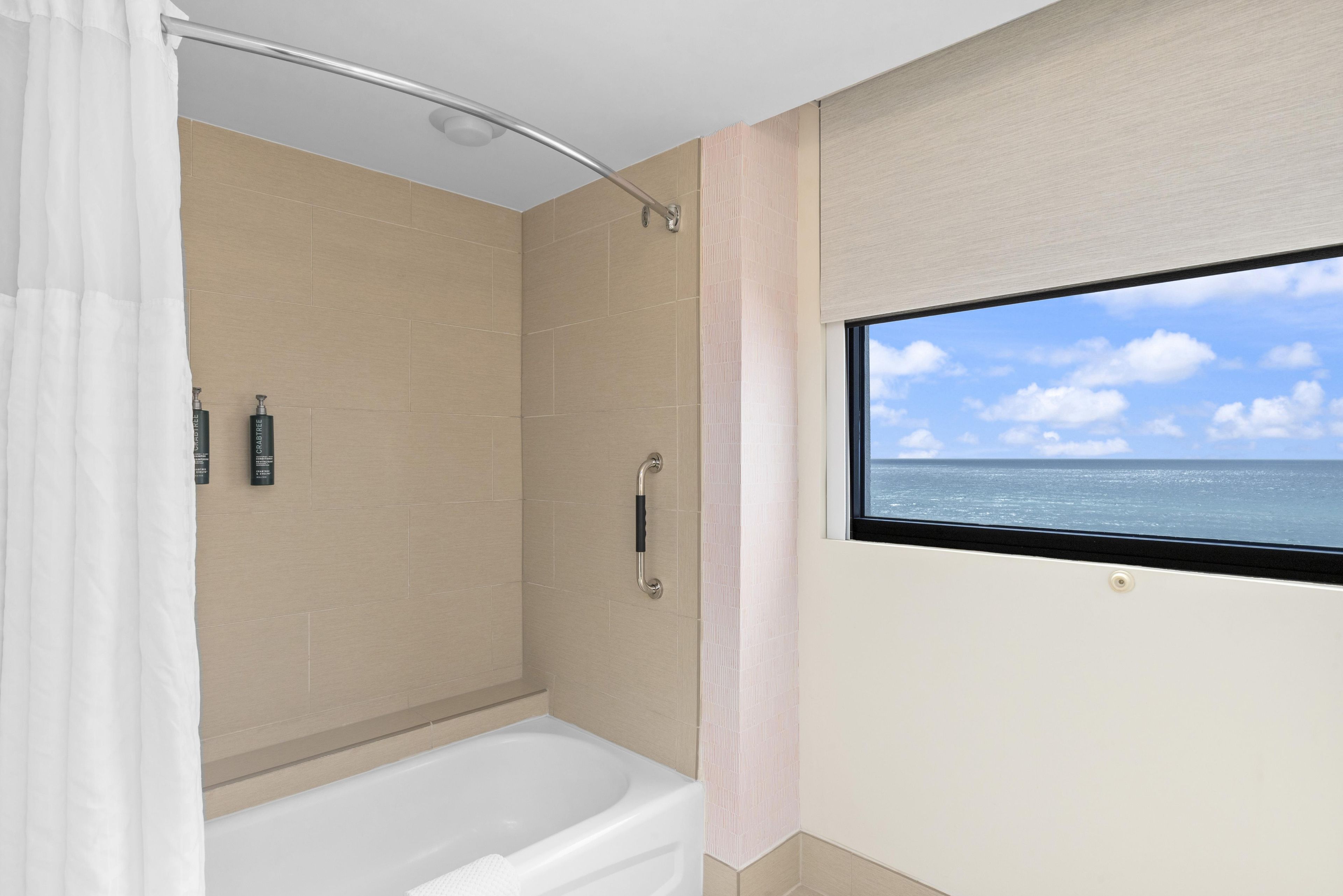 Un baño con bañera, ducha y ventana con vista al mar.