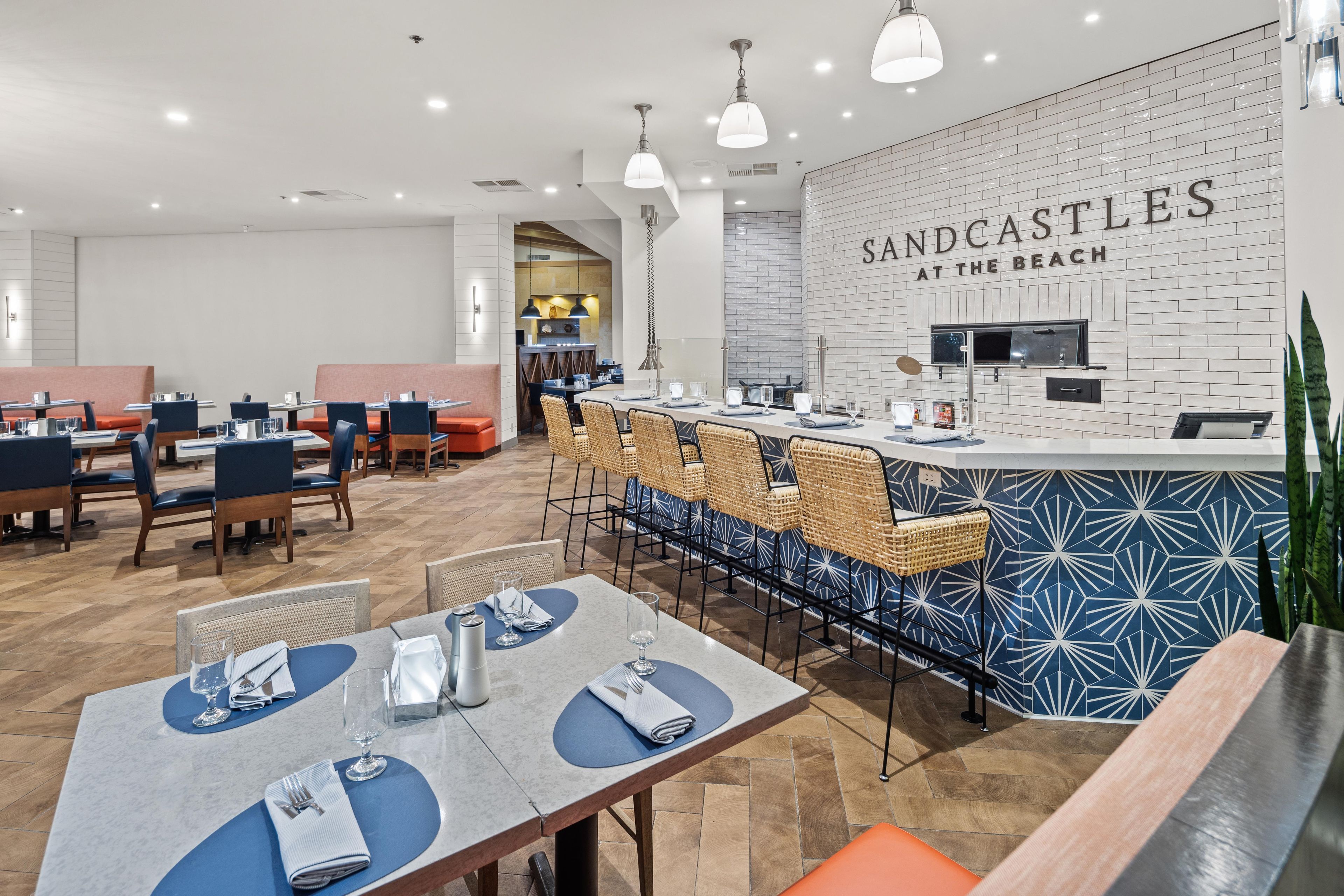 A modern restaurant interior with a bar area, seating arrangements, and a visible kitchen.