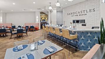 A modern restaurant interior with a bar area, seating arrangements, and a visible kitchen.
