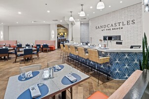 Un interior de restaurante moderno con una zona de bar, disposición de mesas y una cocina a la vista.