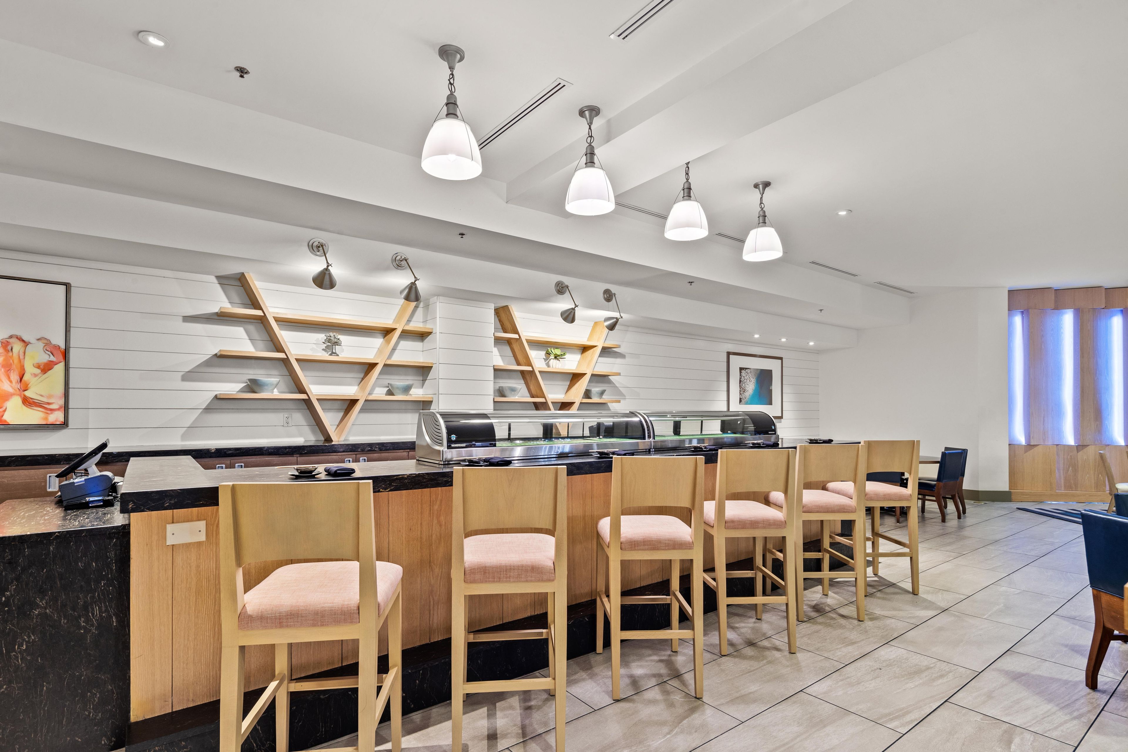 A modern bar area with a long counter, multiple bar stools, pendant lighting, and a decorative wall with shelves.