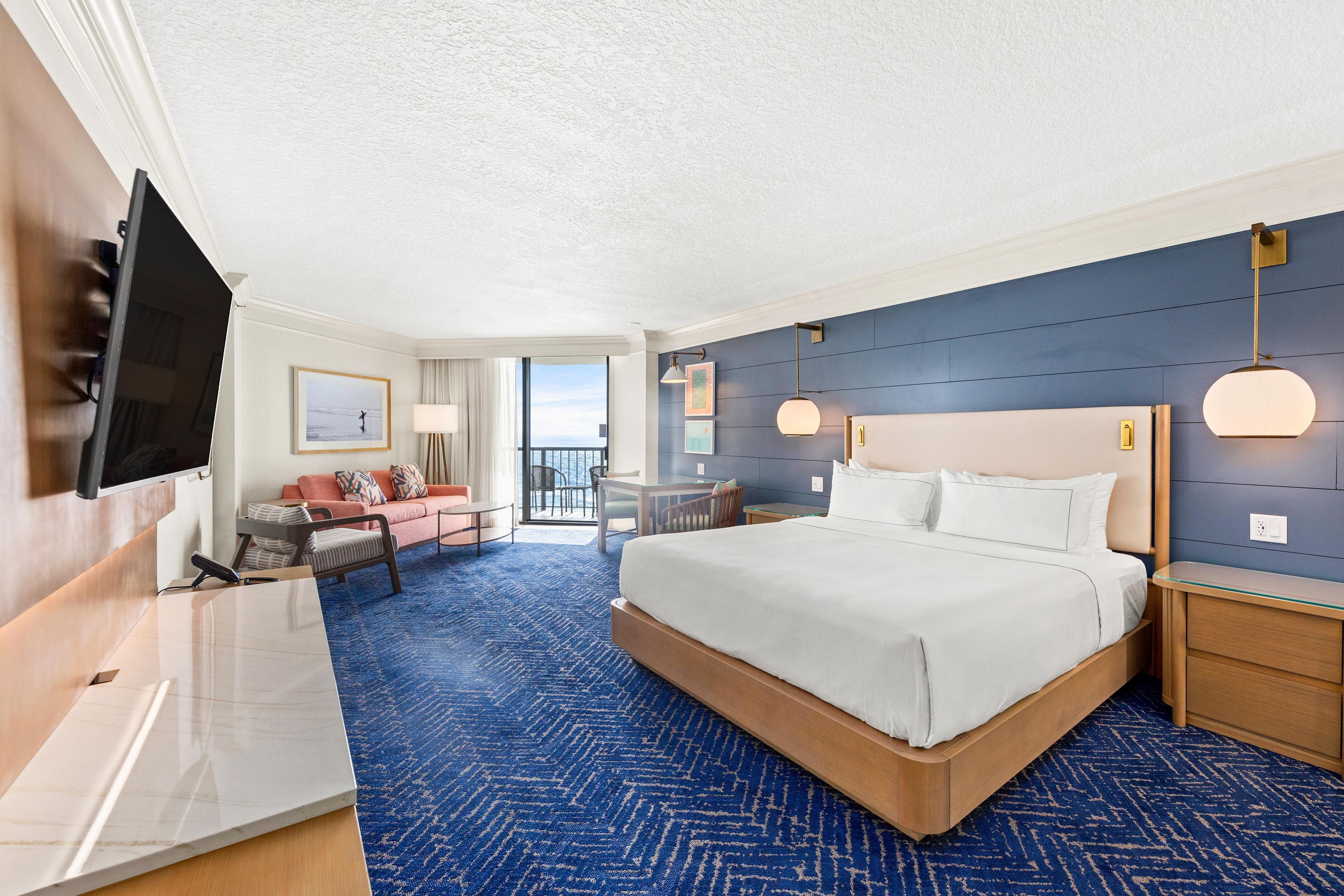 Une chambre d’hôtel avec un grand lit, un bureau, une télévision et une vue sur l’océan.