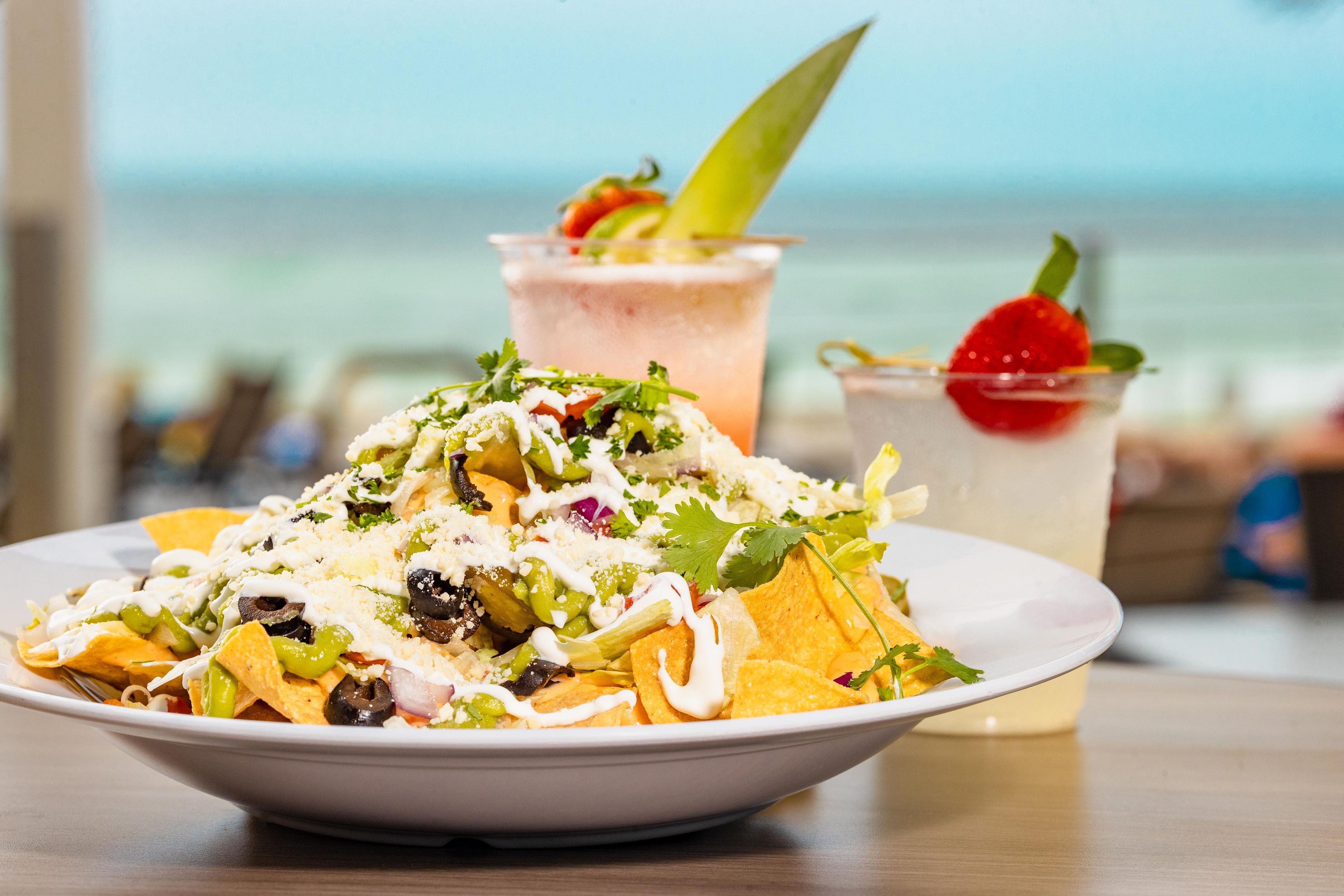 A plate of nachos with toppings and a drink with a strawberry garnish.