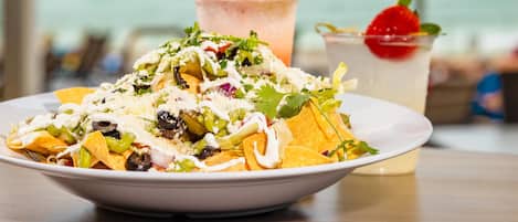 A plate of nachos with toppings and a drink with a strawberry garnish.
