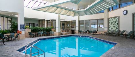 An indoor swimming pool with a clear view of the ceiling structure, lounge chairs, and a clock on the wall.
