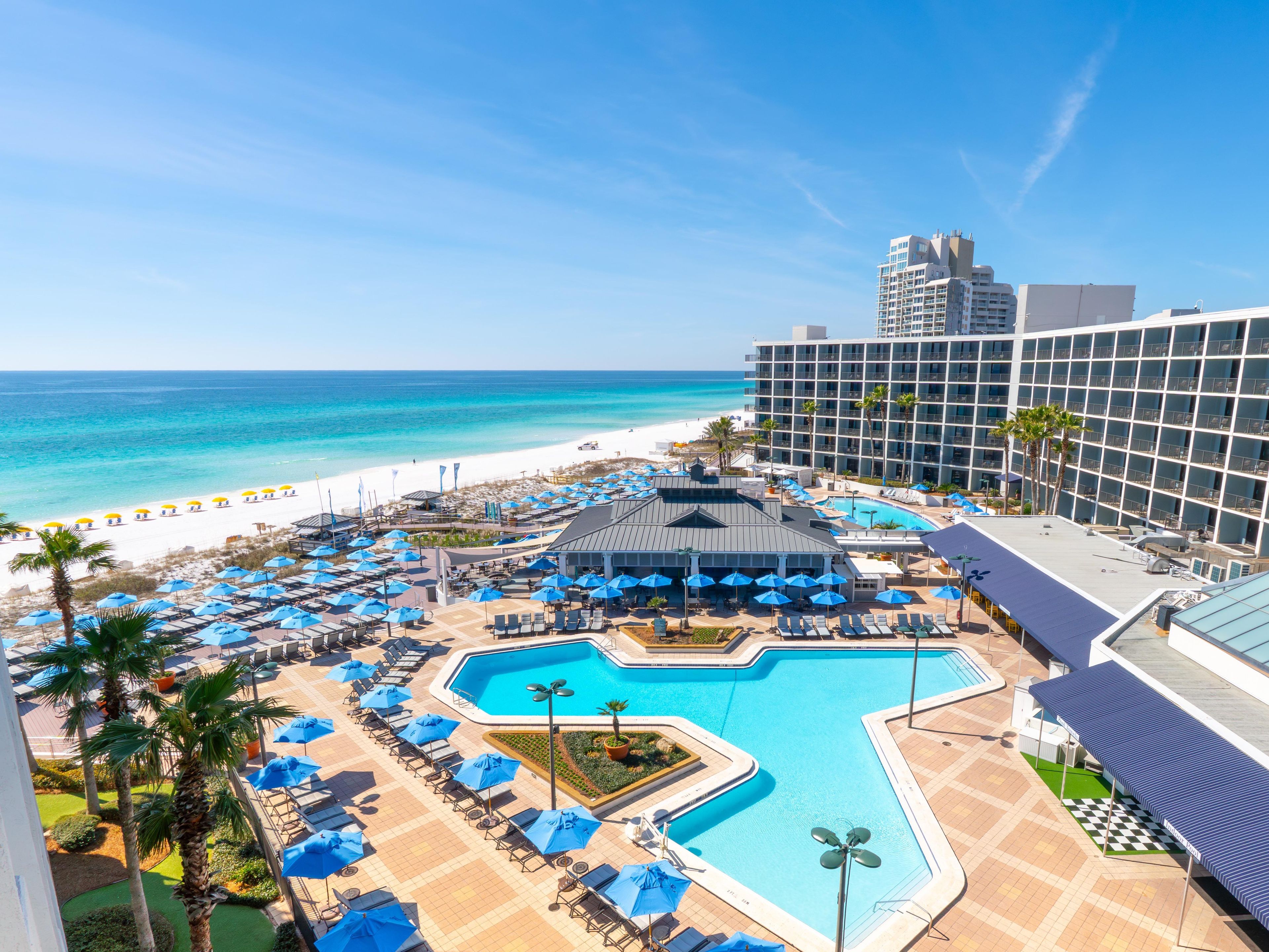 A resort with a swimming pool, beach umbrellas, and a view of the ocean.