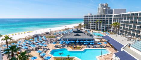 A resort with a swimming pool, beach umbrellas, and a view of the ocean.