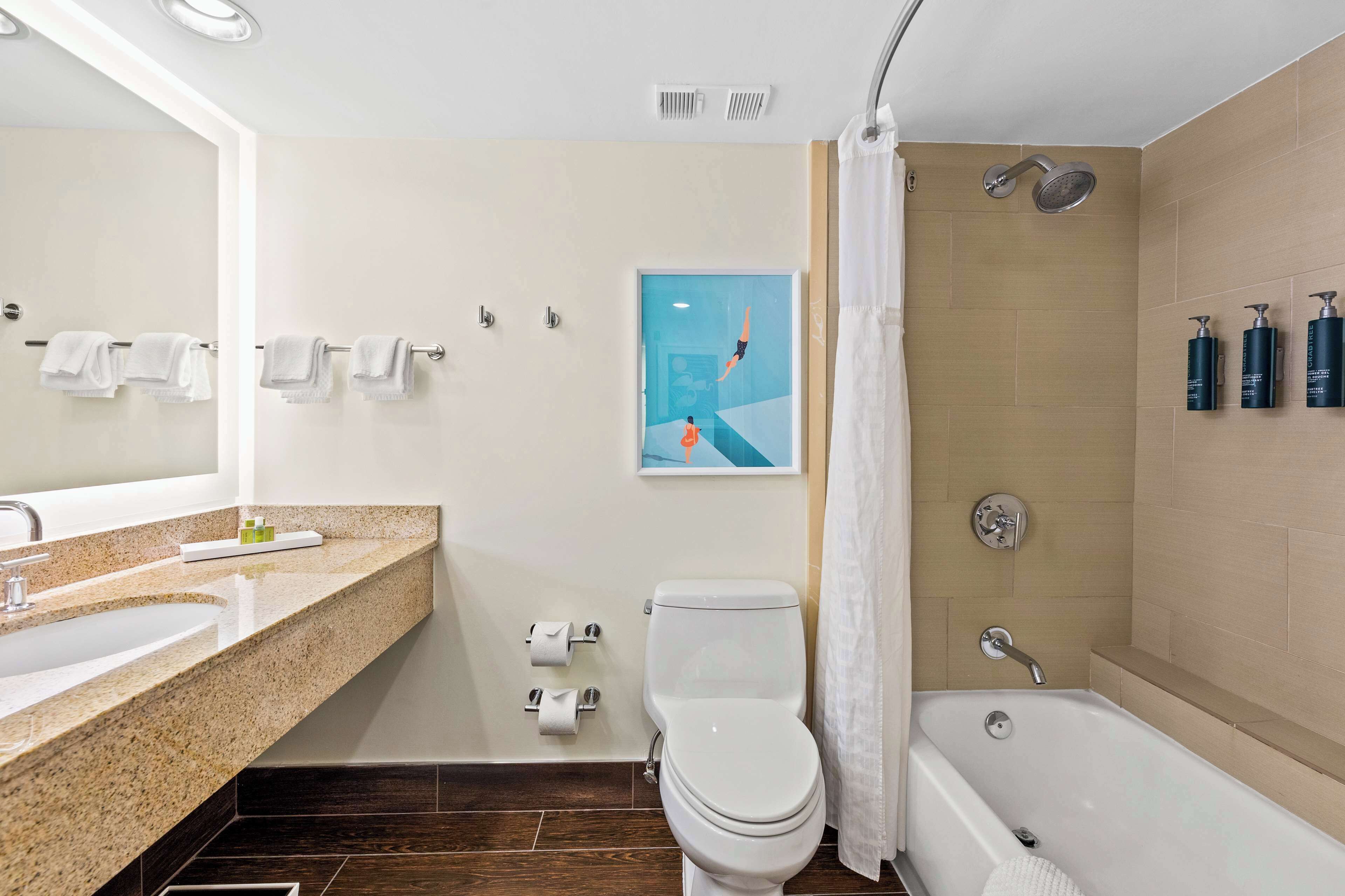 Ein modernes Badezimmer mit Waschbecken, Toilette, Badewanne und Dusche. Handtücher hängen an der Wand und ein Bild zeigt einen Taucher.