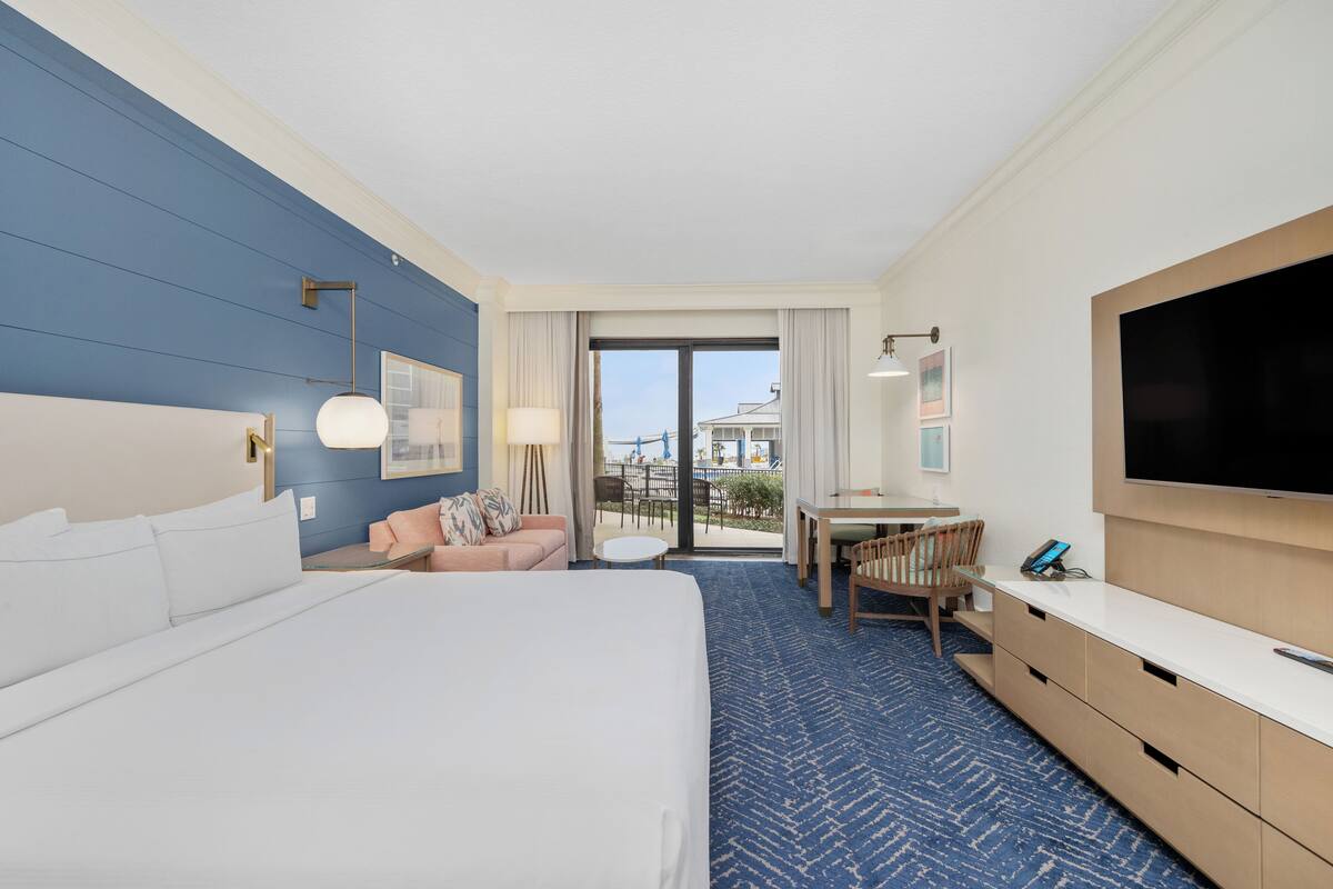 A hotel room with a large bed, a sofa, a desk, and a television.