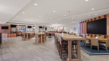 A spacious indoor area with multiple seating arrangements, a bar area, and a large screen.