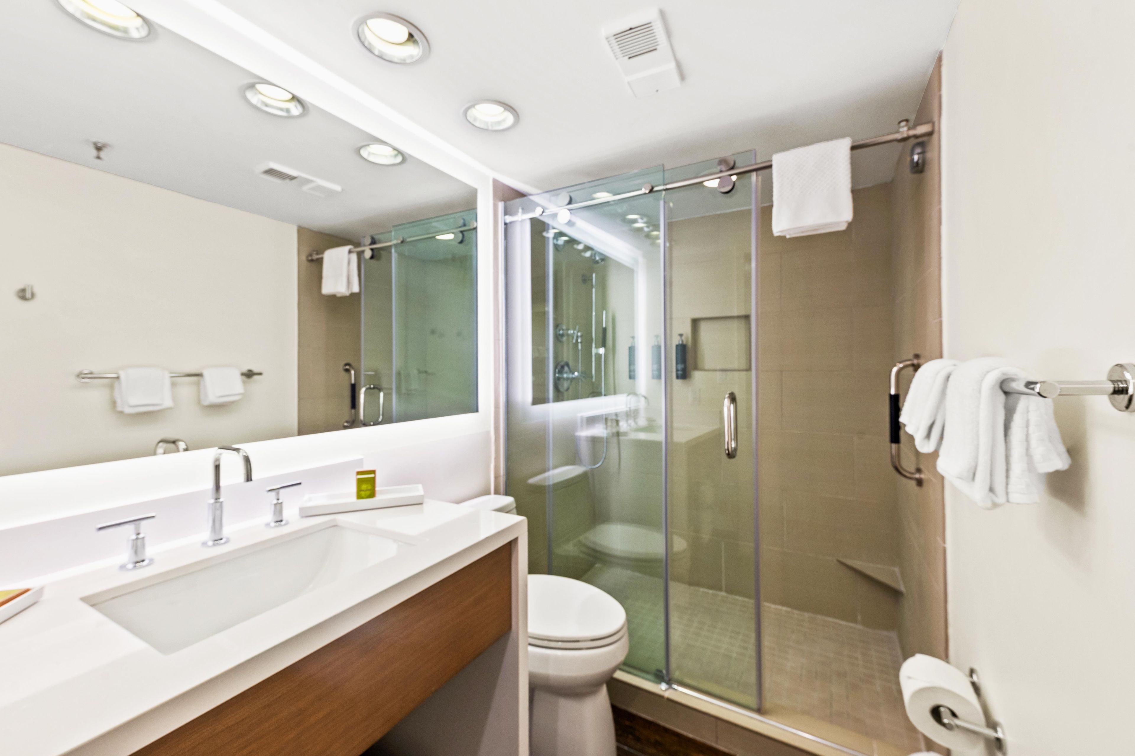 A modern bathroom with a glass-enclosed shower, a large mirror, and a white sink.