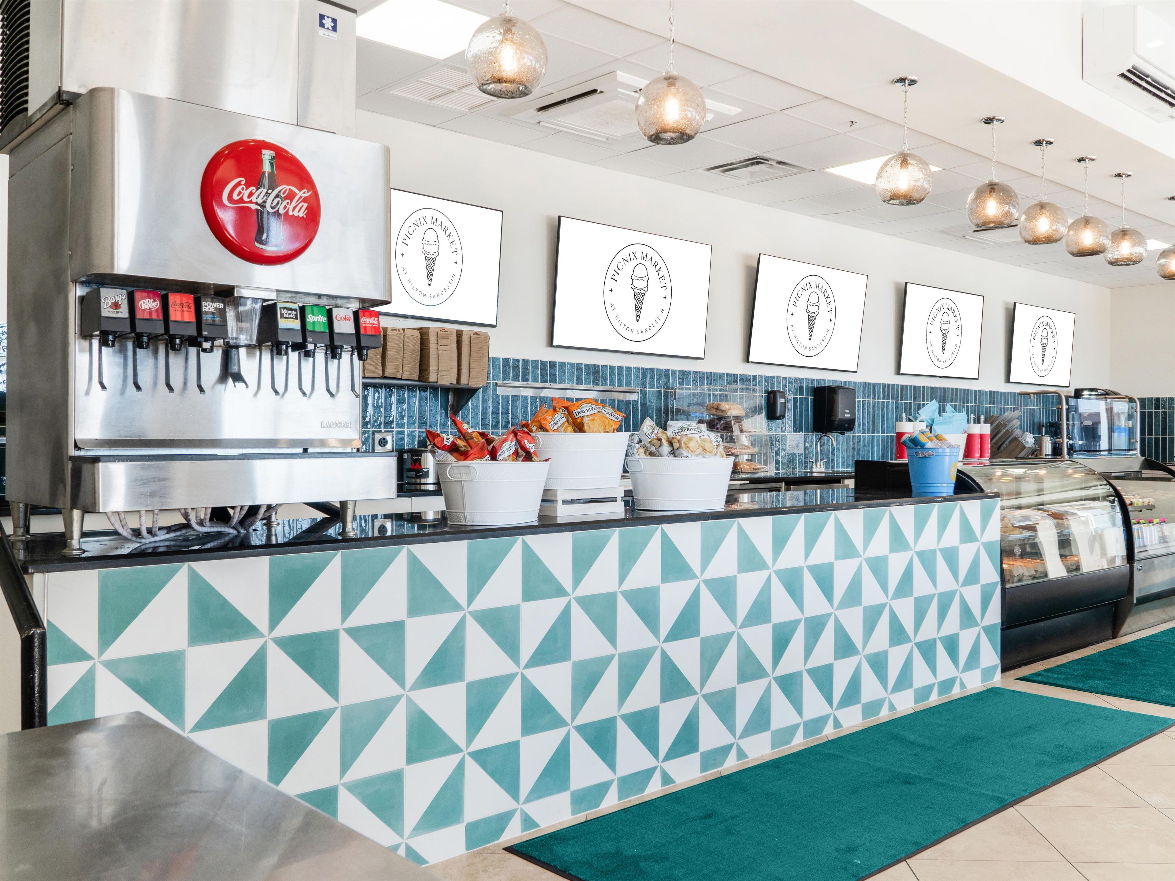 A cafe with a Coca-Cola machine, a Picnix Market sign, and a counter with food items.