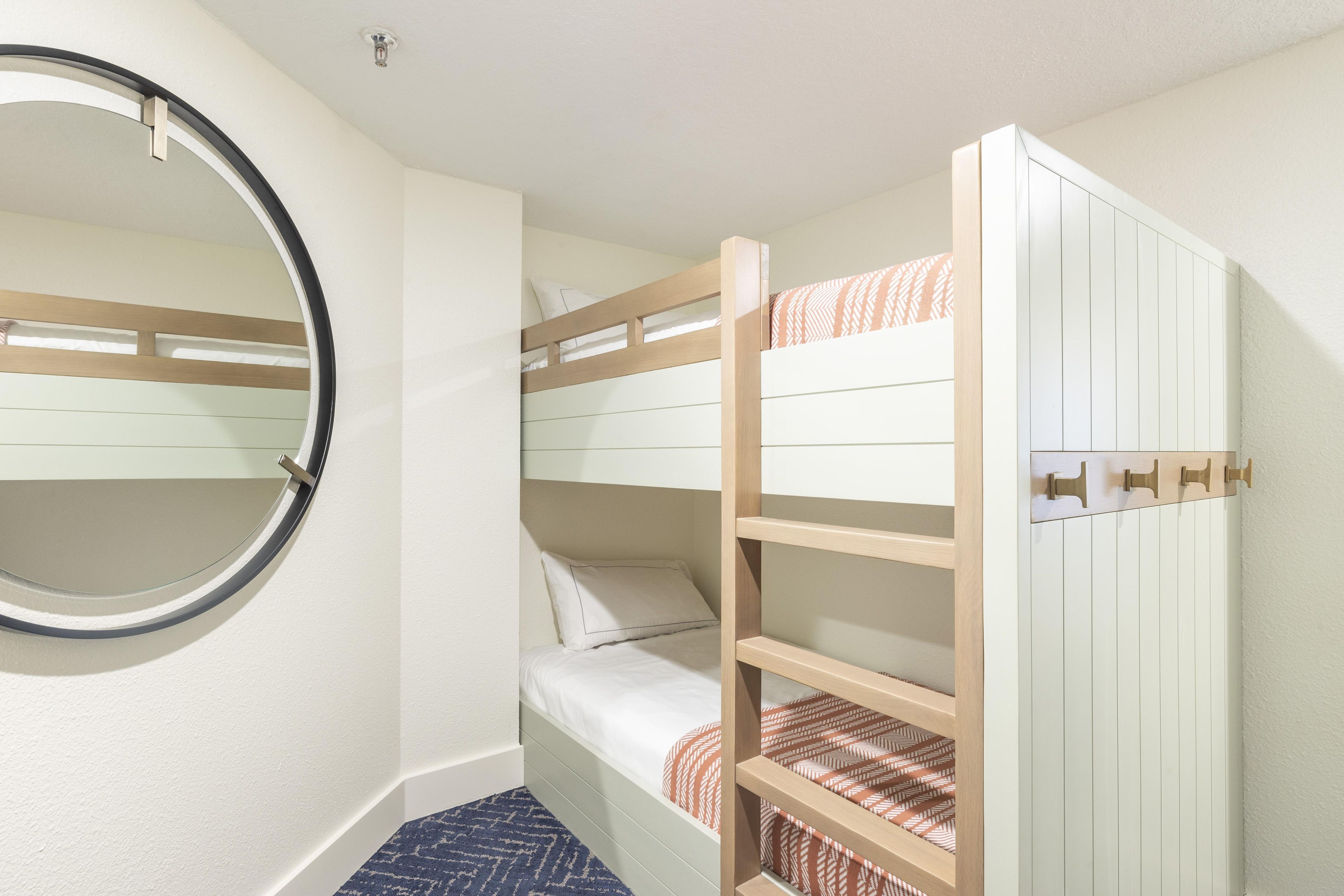 A bunk bed room with a circular mirror on the wall, a small bedside table, and a patterned rug.