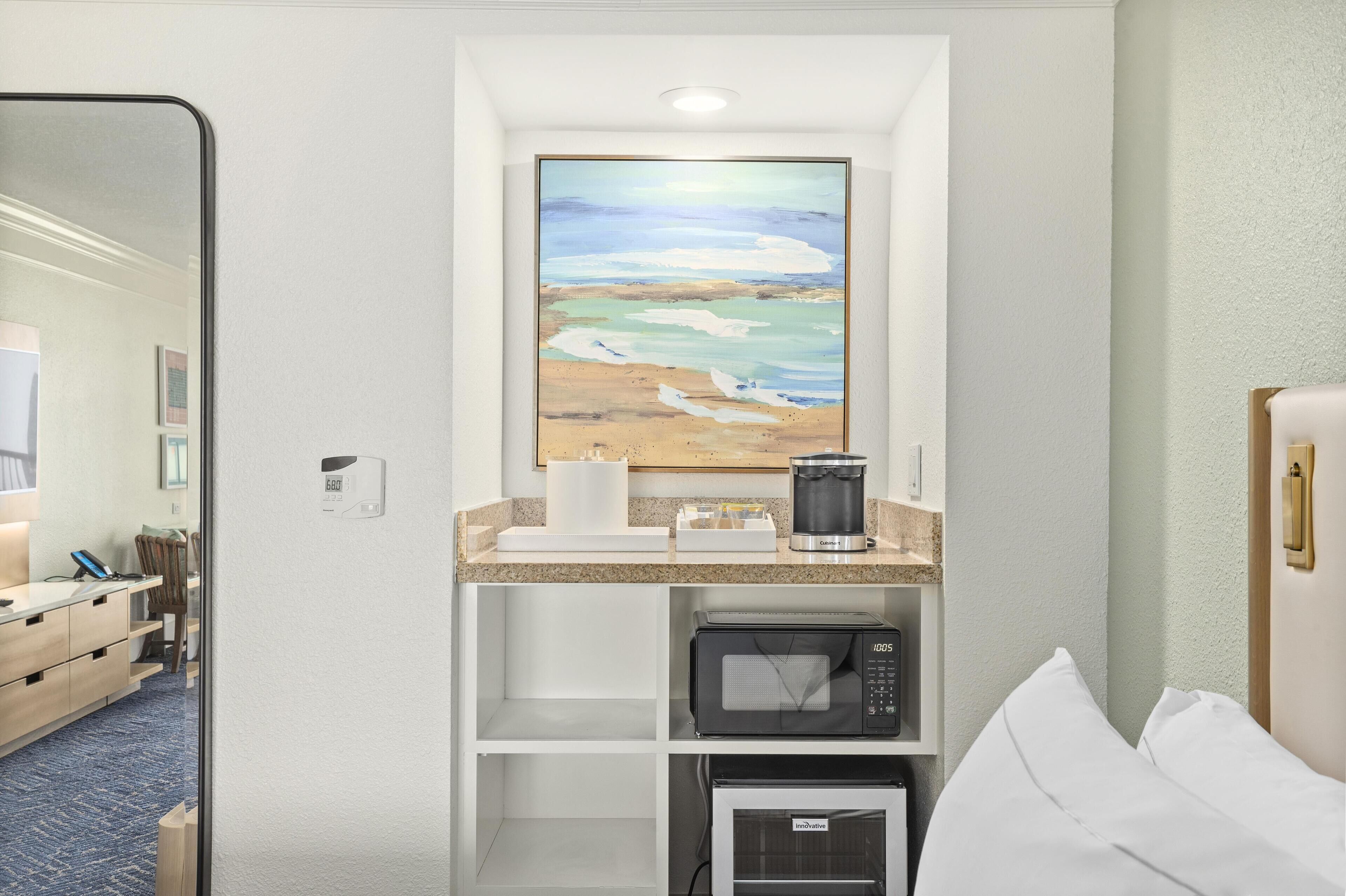 Habitación de hotel con un cuadro de una playa, una cafetera, un microondas y una cama.