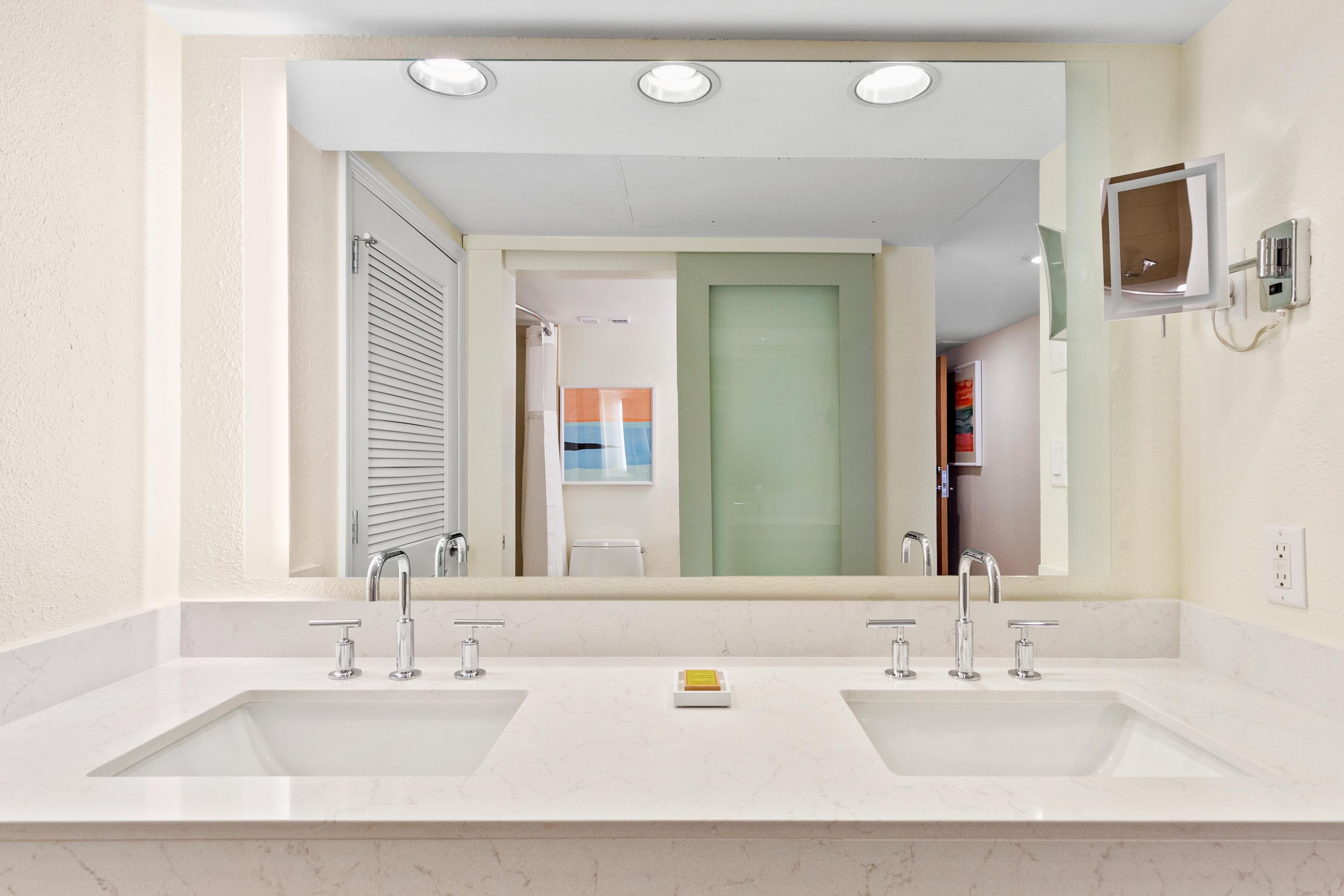 A bathroom with two sinks, a large mirror, and a shower.
