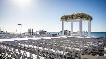 An outdoor wedding venue with white chairs arranged in rows, a white arch with floral decorations, and a view of the ocean.