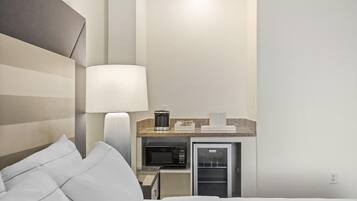 A hotel room with a bed, a bedside lamp, a microwave, and a refrigerator.