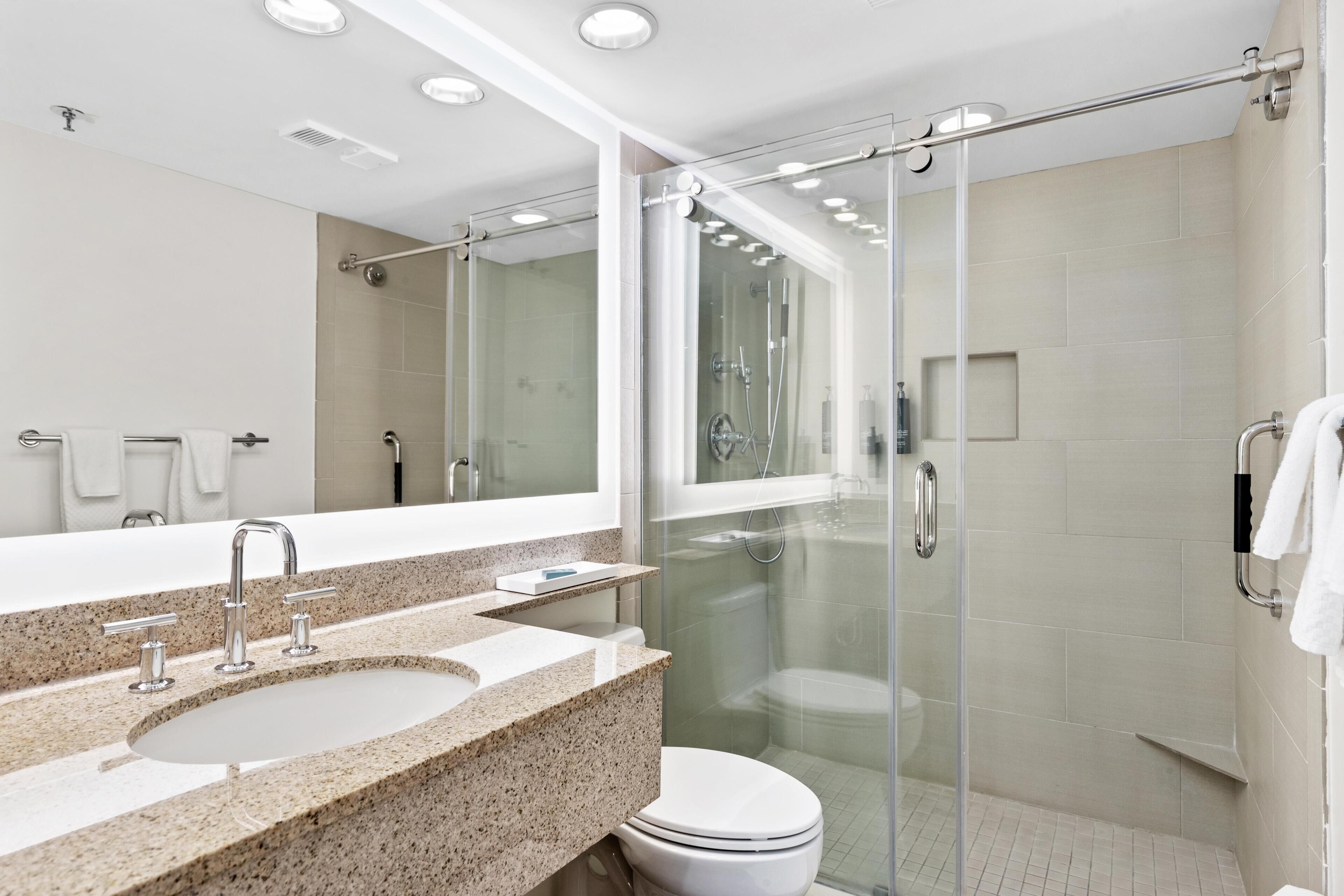 A modern bathroom with a granite countertop sink, a glass shower enclosure, and a white toilet.