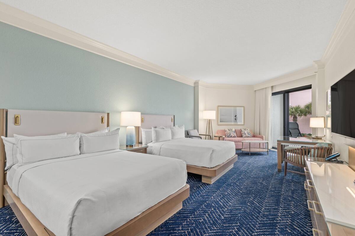 A hotel room with two beds, a desk, a chair, a sofa, and a TV.