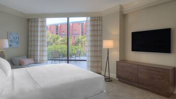 Een hotelkamer met een bed, een flatscreen televisie, een bureau met een lamp en uitzicht op gebouwen en groen.