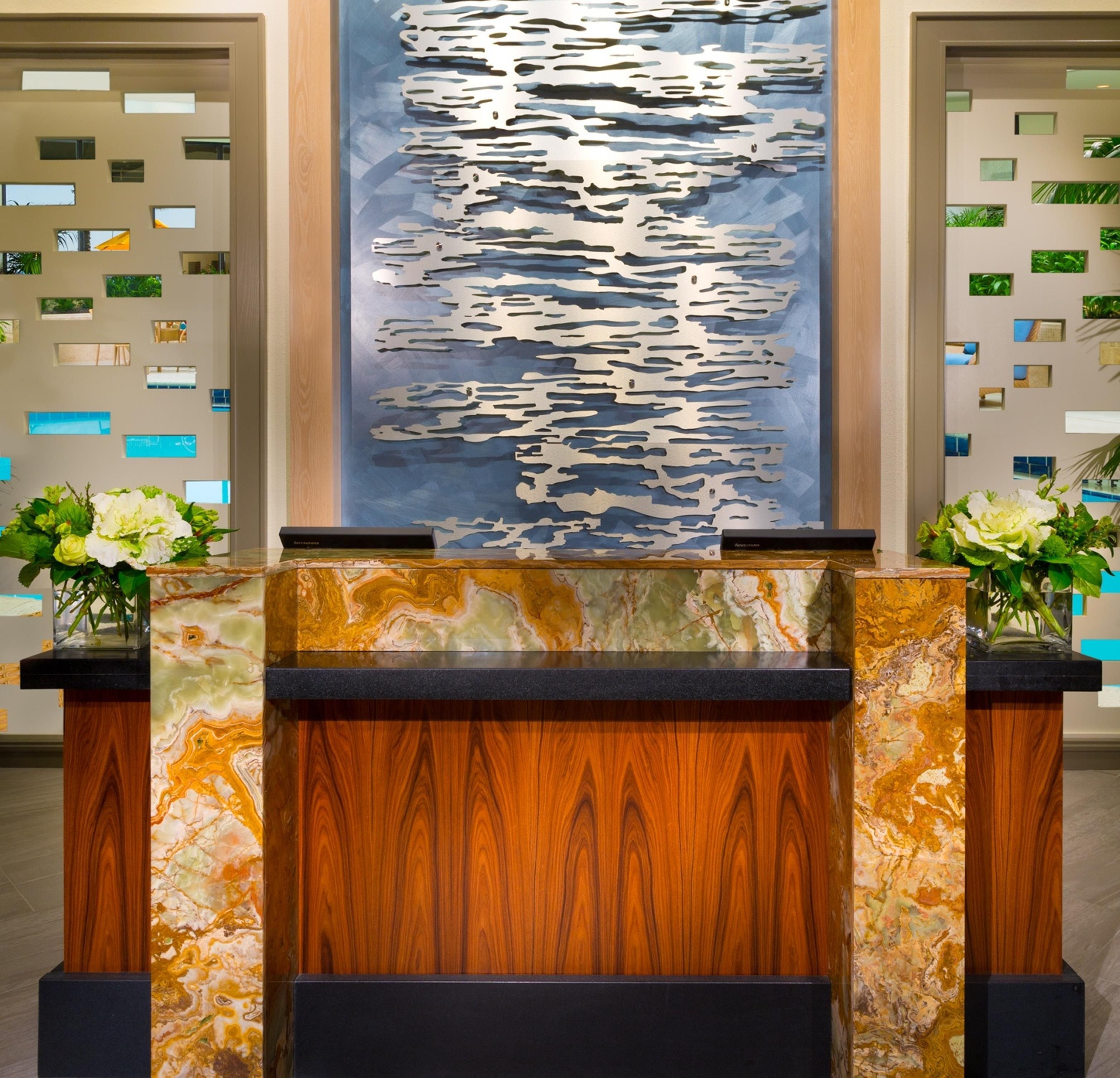 A reception desk with a marble top and wooden base, flanked by two vases with flowers. Behind the desk is a wall with a large abstract painting and a series of framed pictures.