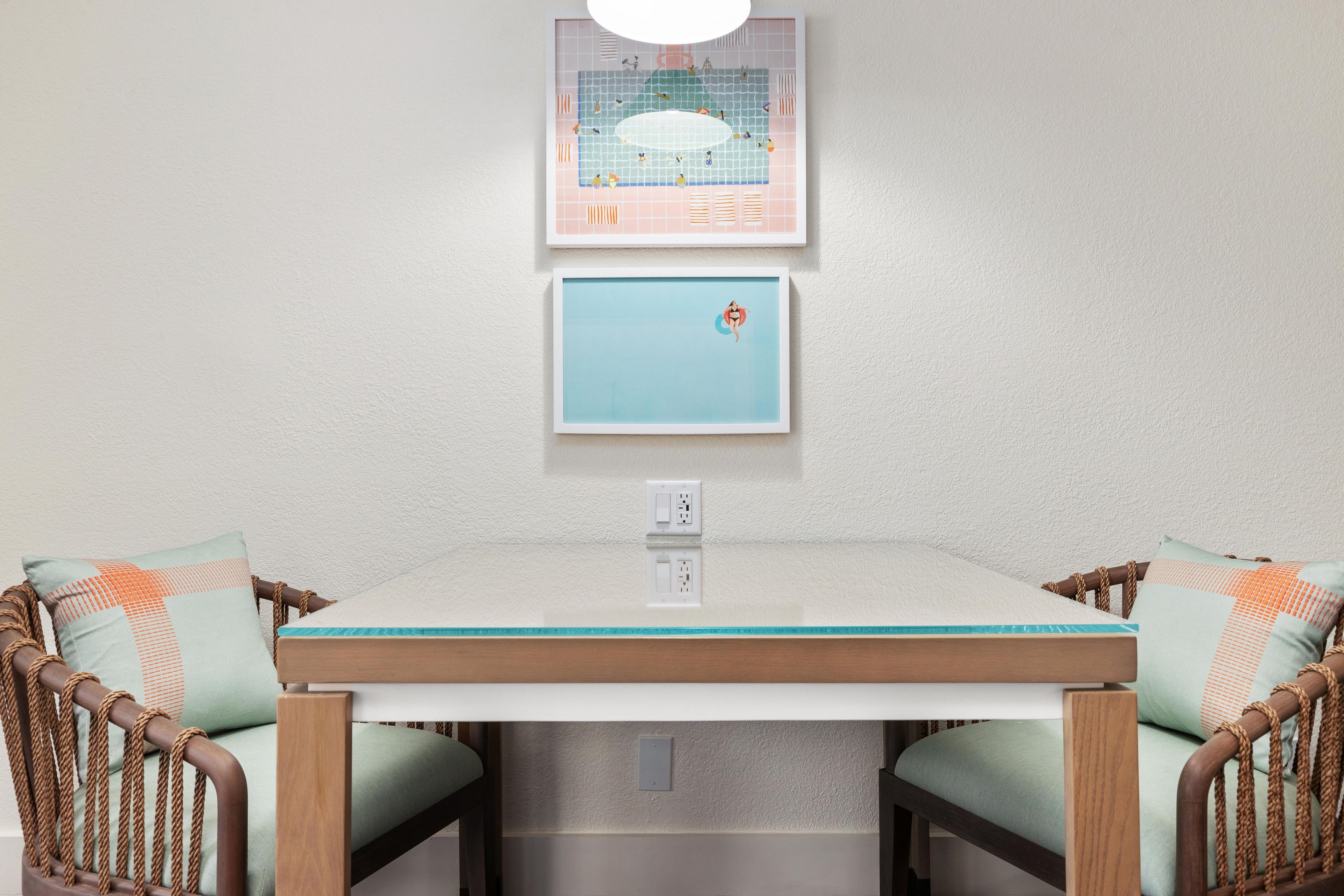 A dining area with a table, chairs, and two framed pictures on the wall.