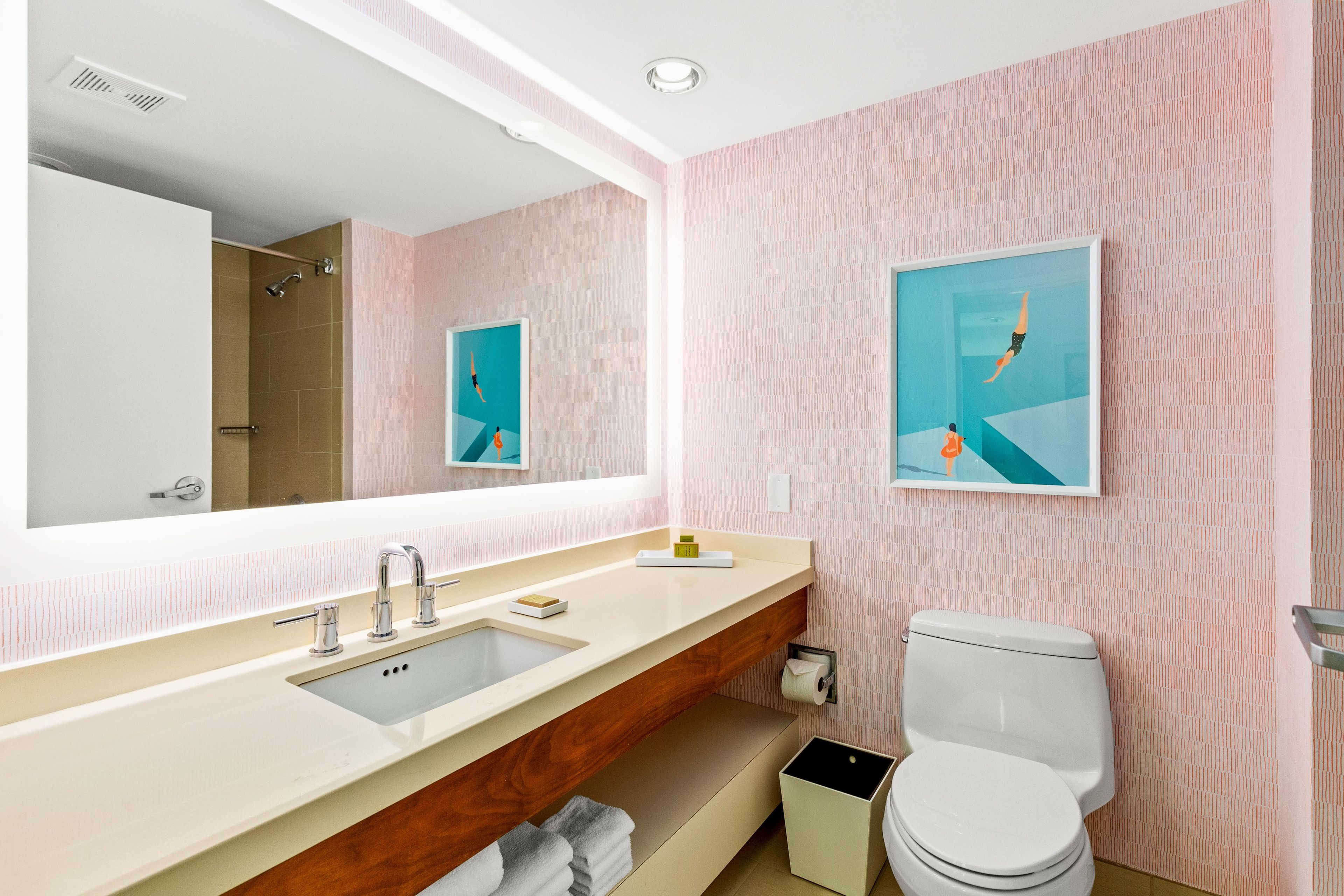 A modern bathroom with a large mirror, a sink, a toilet, and two framed pictures on the wall.