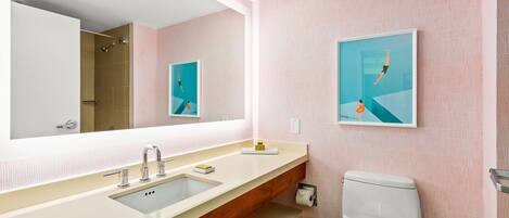 A modern bathroom with a large mirror, a sink, a toilet, and two framed pictures on the wall.