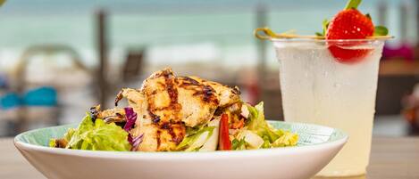 Un tazón de ensalada con pollo a la parrilla y un vaso de bebida helada, adornado con fresas.