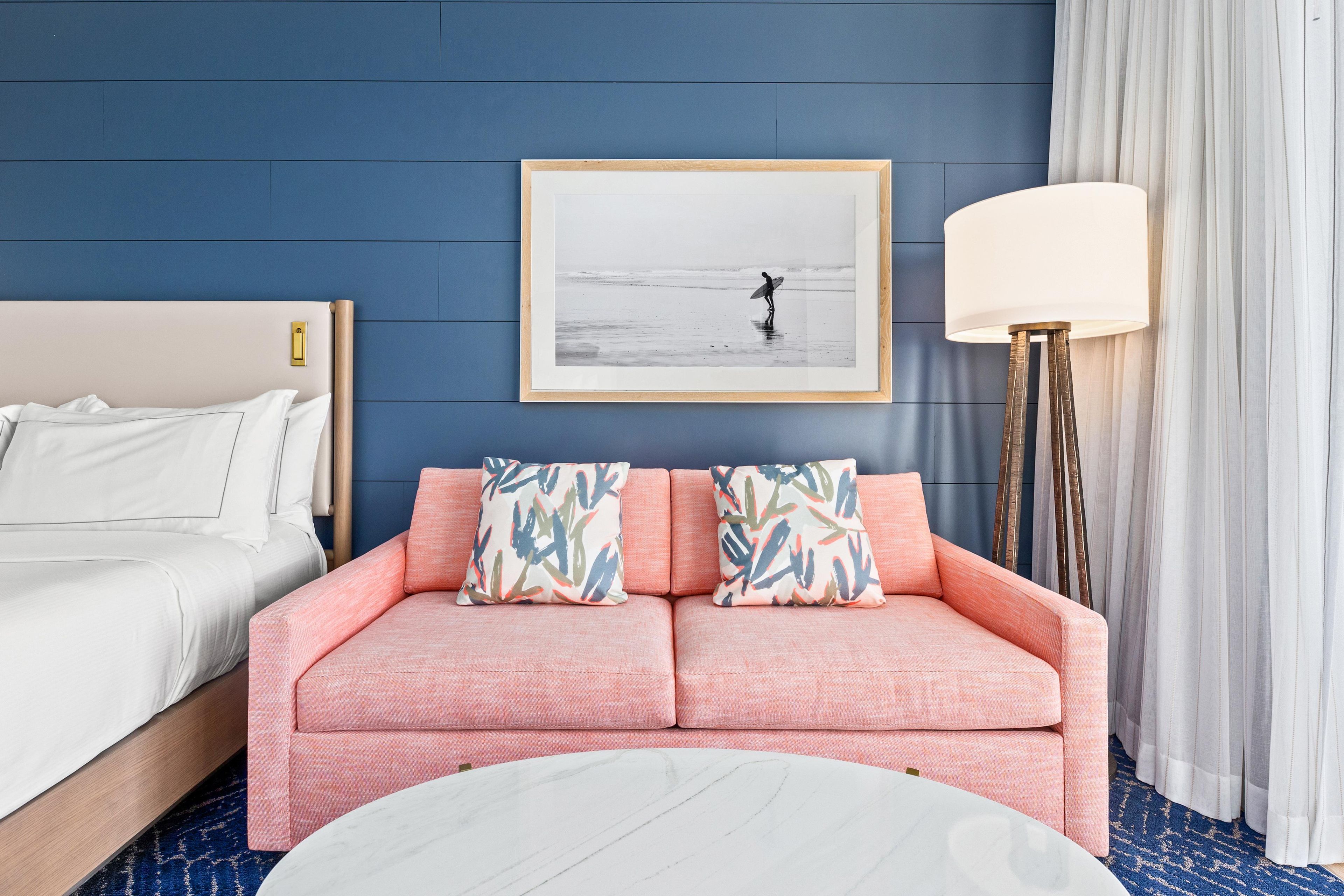 Une chambre d’hôtel avec un lit, un canapé, un tableau encadré au mur et une lampe sur pied.