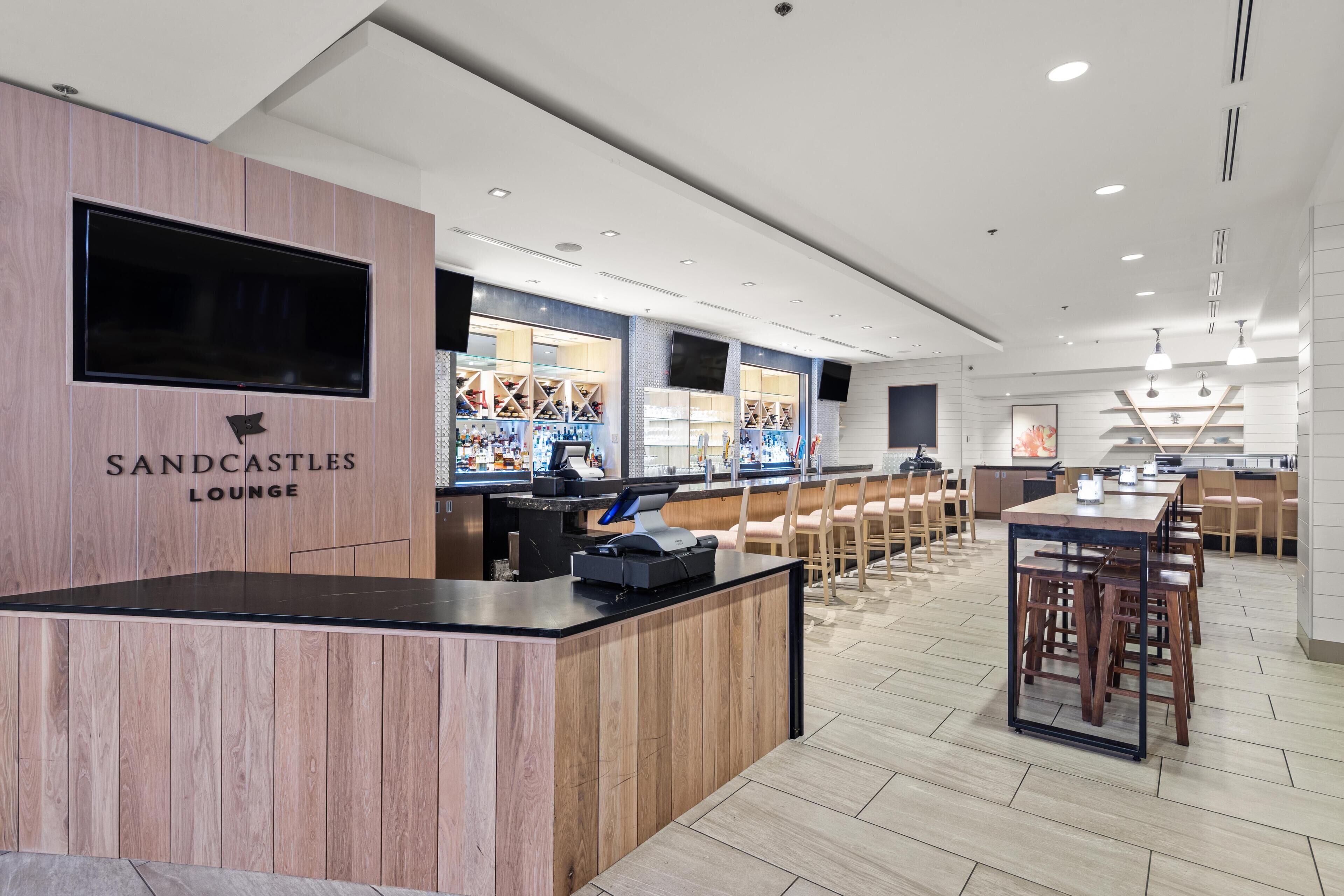A modern lounge area with a reception desk, seating, and a large TV screen.