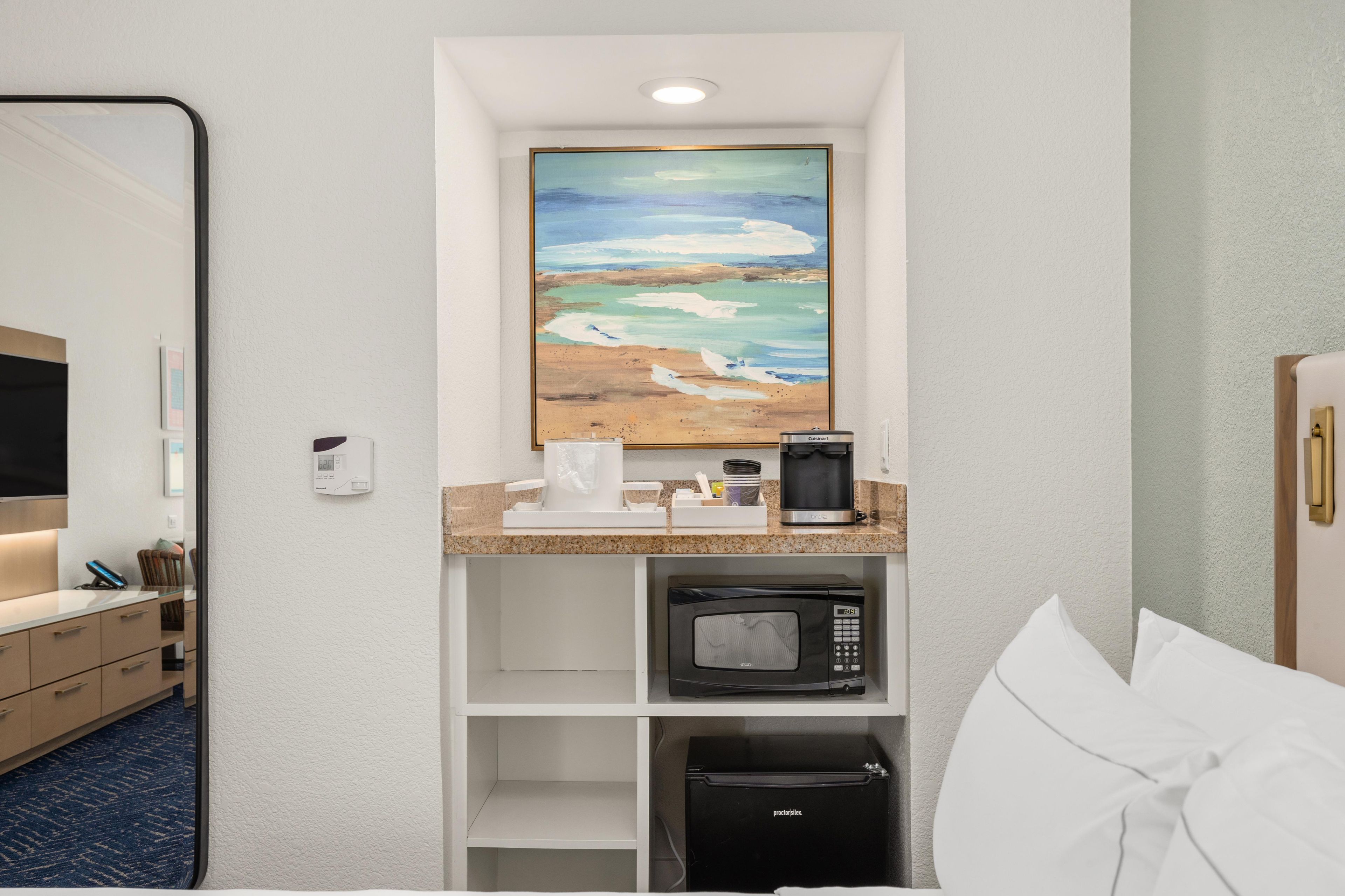 Une chambre d’hôtel avec une kitchenette, un tableau représentant une scène de plage, un four à micro-ondes et un réfrigérateur.