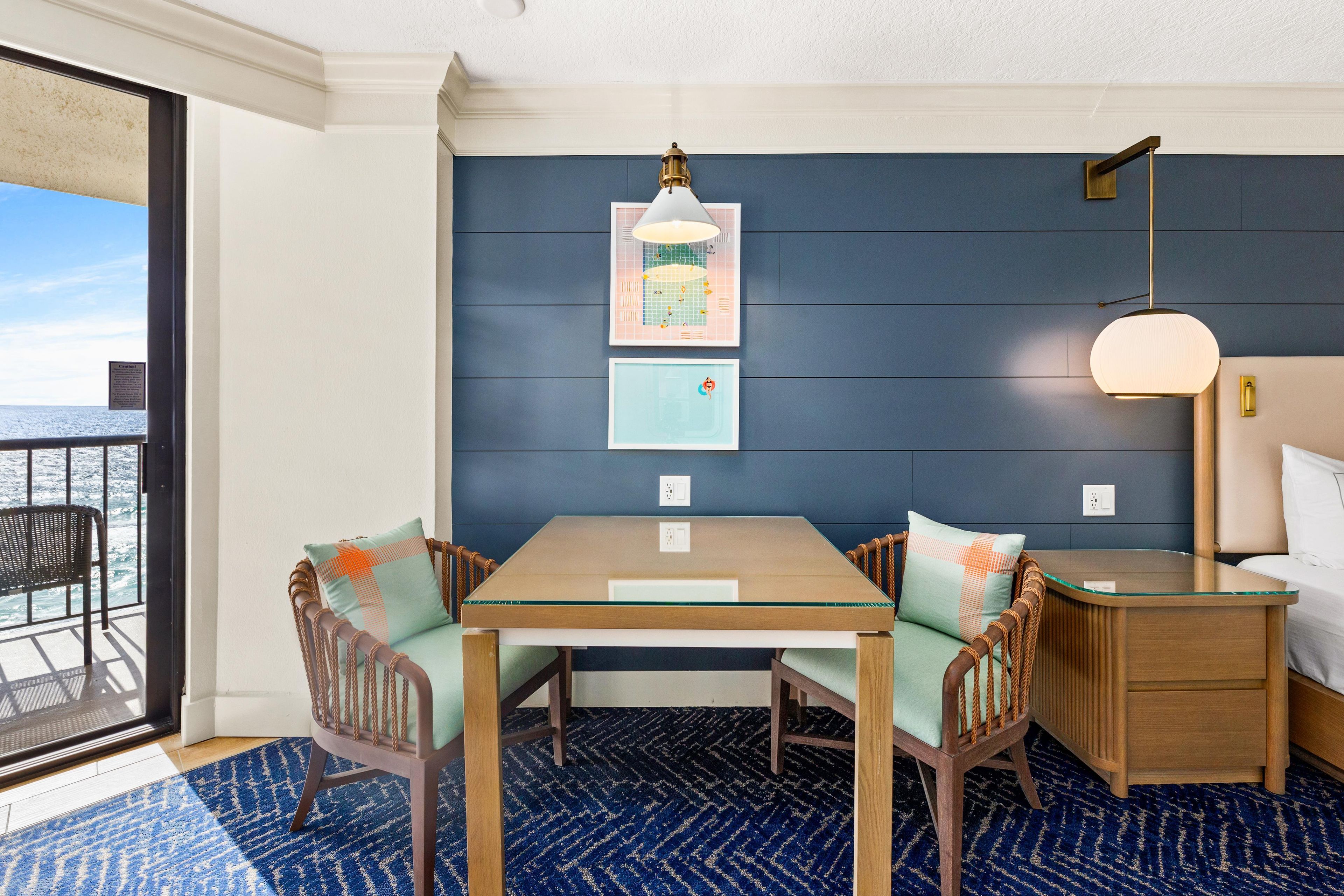 Una habitación con una mesa de comedor, dos sillas, una cama, una mesita de noche y una pared con dos cuadros enmarcados.