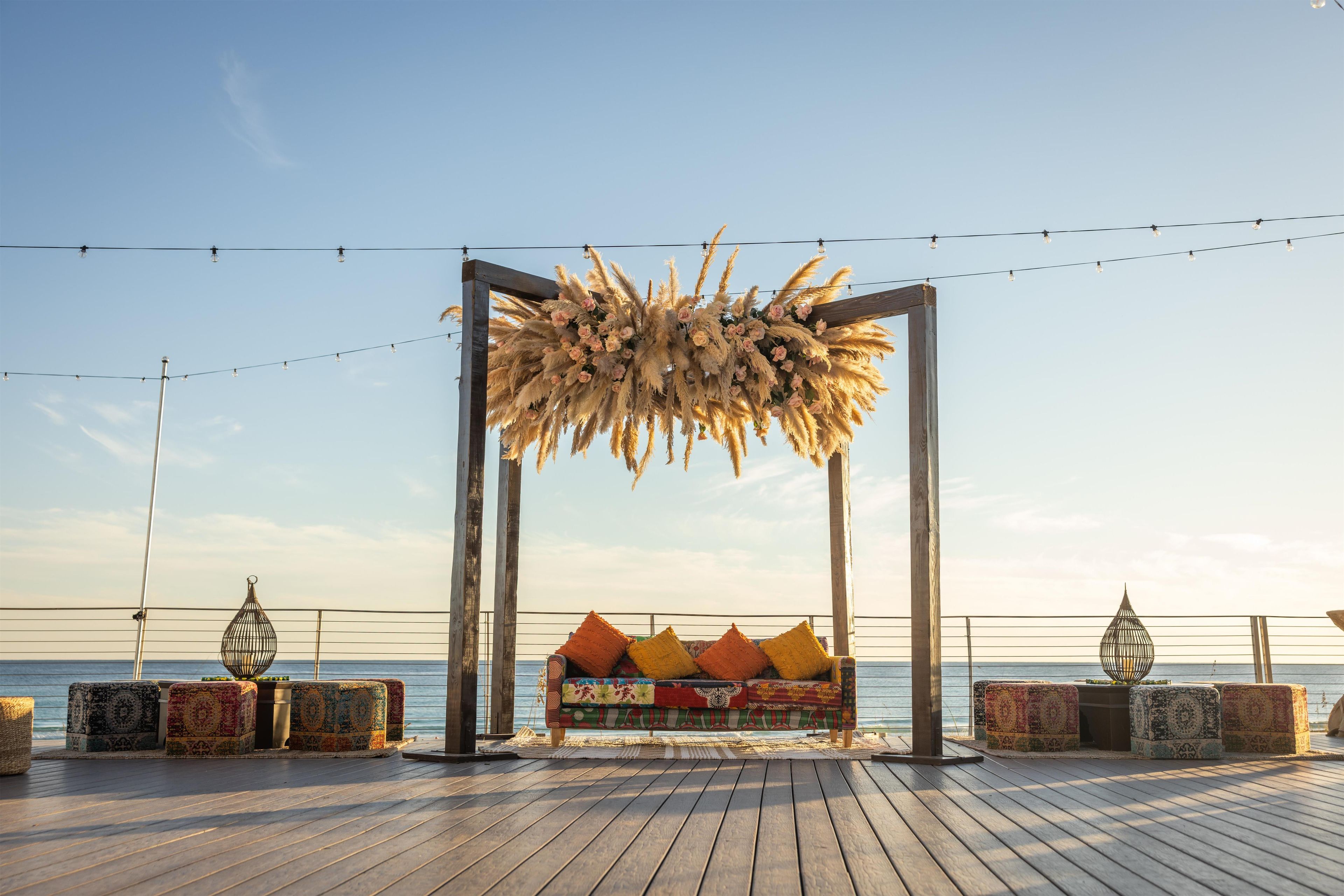 An outdoor seating area with a wooden deck, a bench with colorful cushions, and a decorative floral arrangement above.