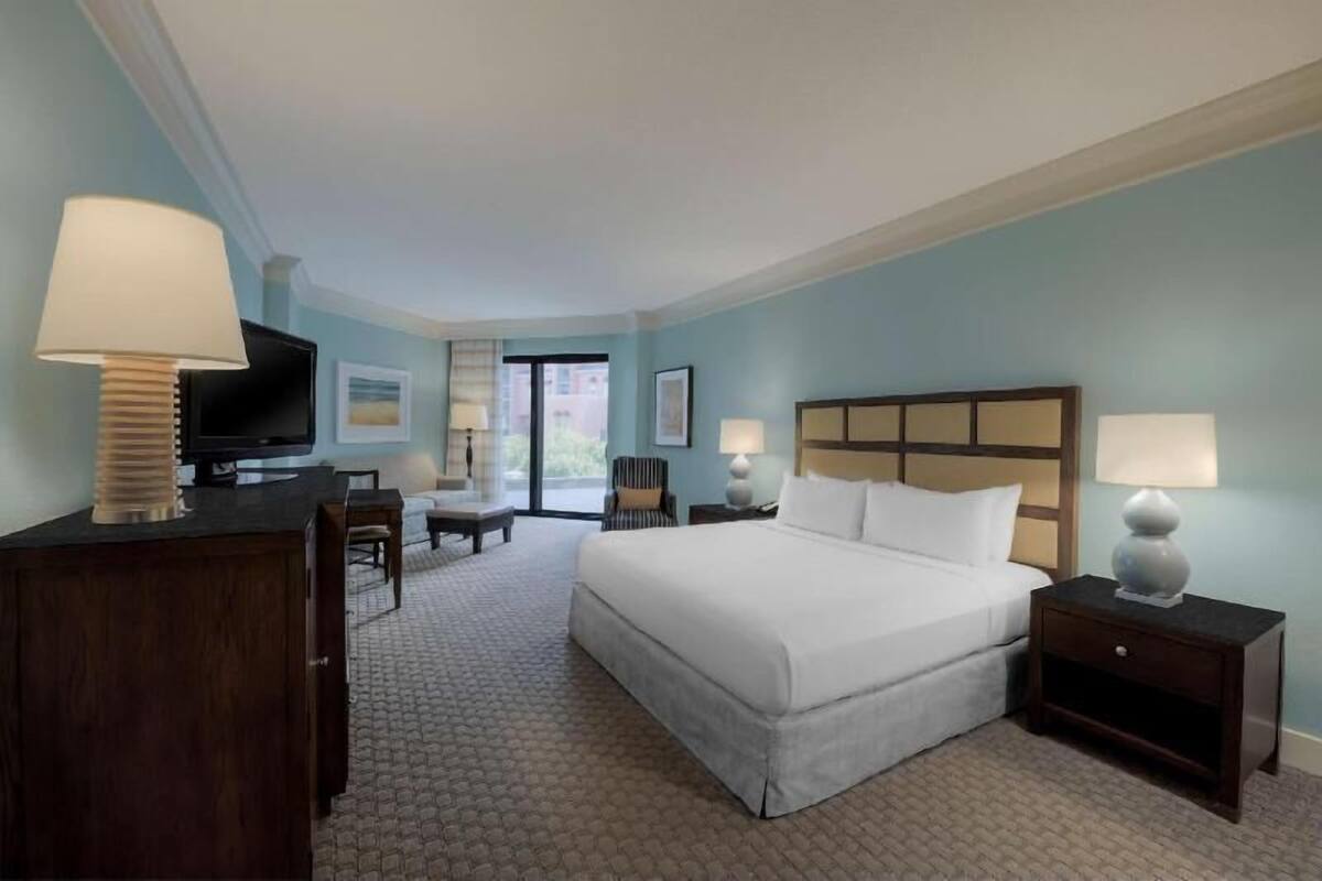A hotel room with a bed, a desk, a chair, a television, and a window.